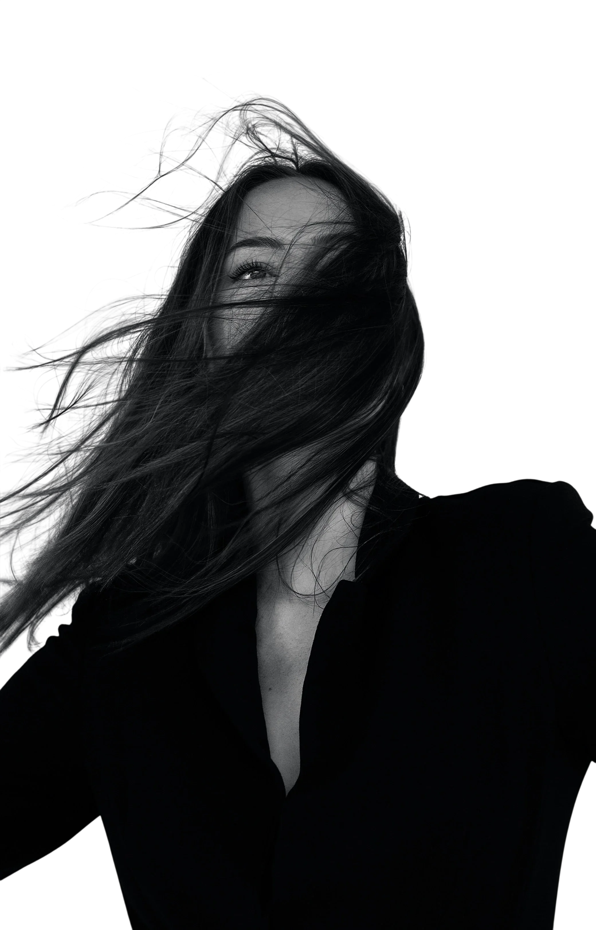 Black and white photo of a woman with long hair covering part of her face, smiling slightly, against a blurred background.