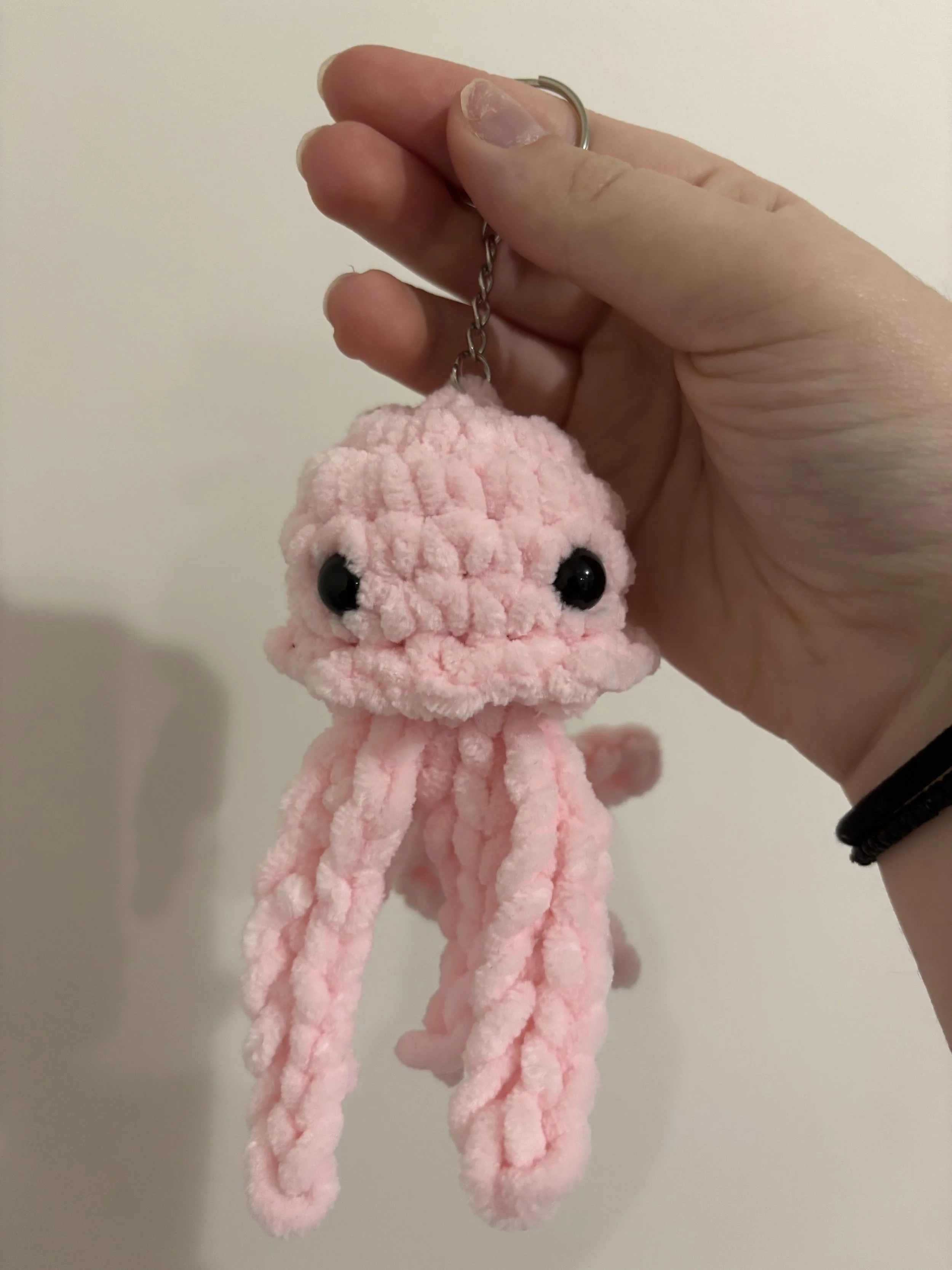 A person holding a pink plush octopus keychain with black eyes against a plain white background.