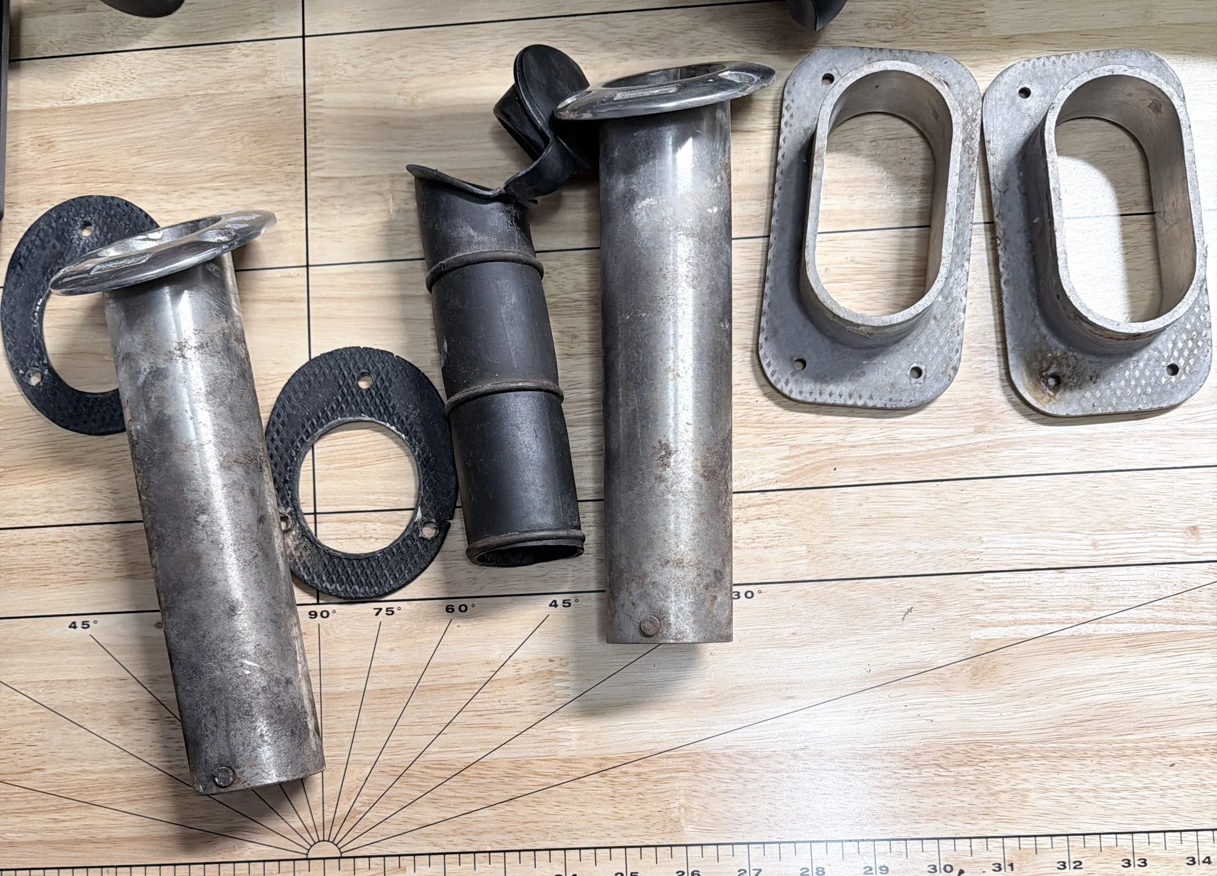 Several metallic pipe fittings and gaskets are laid out on a wooden surface with measurement markings.