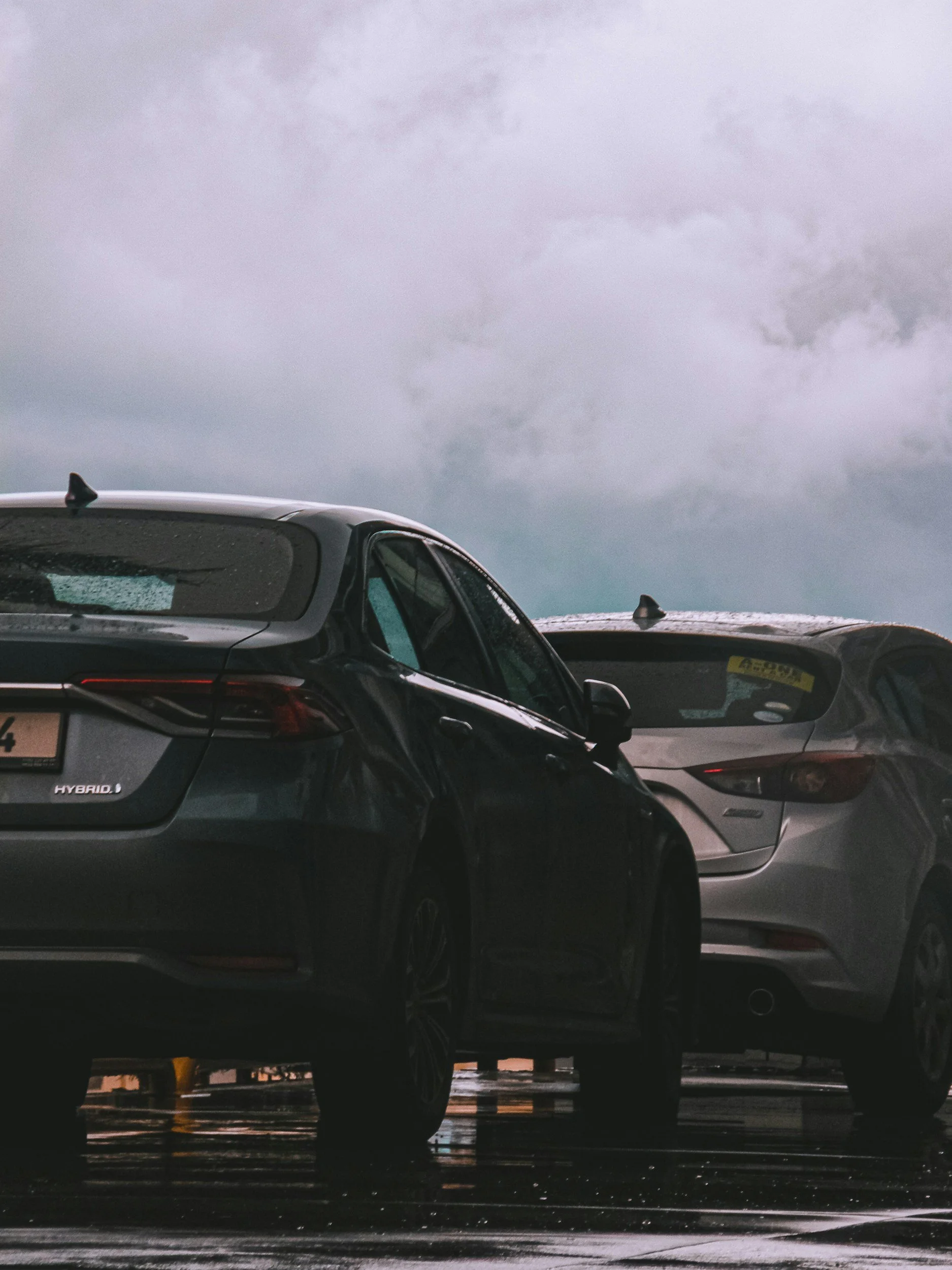 Multiple cars parked in a lot on a rainy day with an overcast sky.