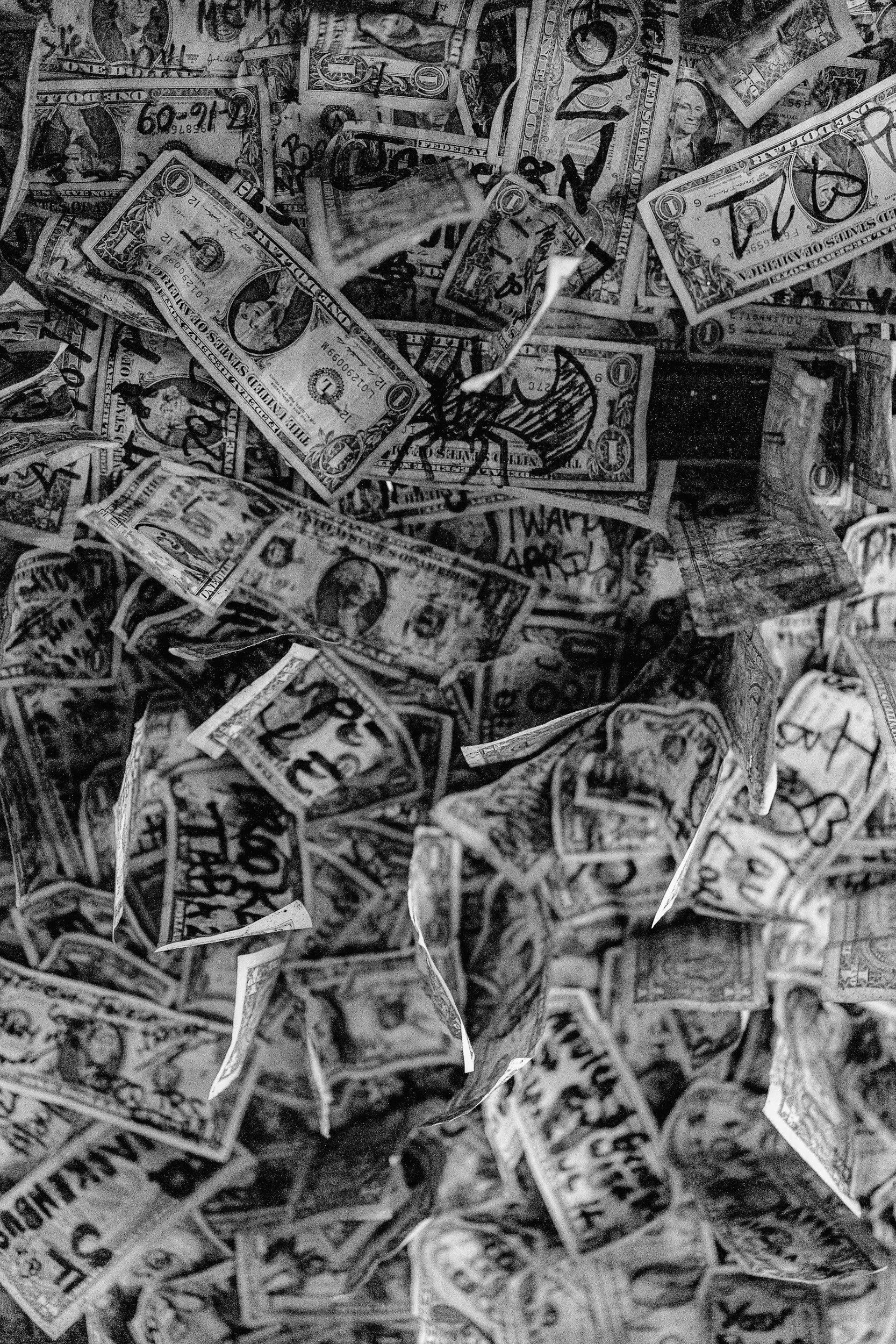 A pile of scattered and crumpled dollar bills and paper currency, with some handwritten words and signs on them.