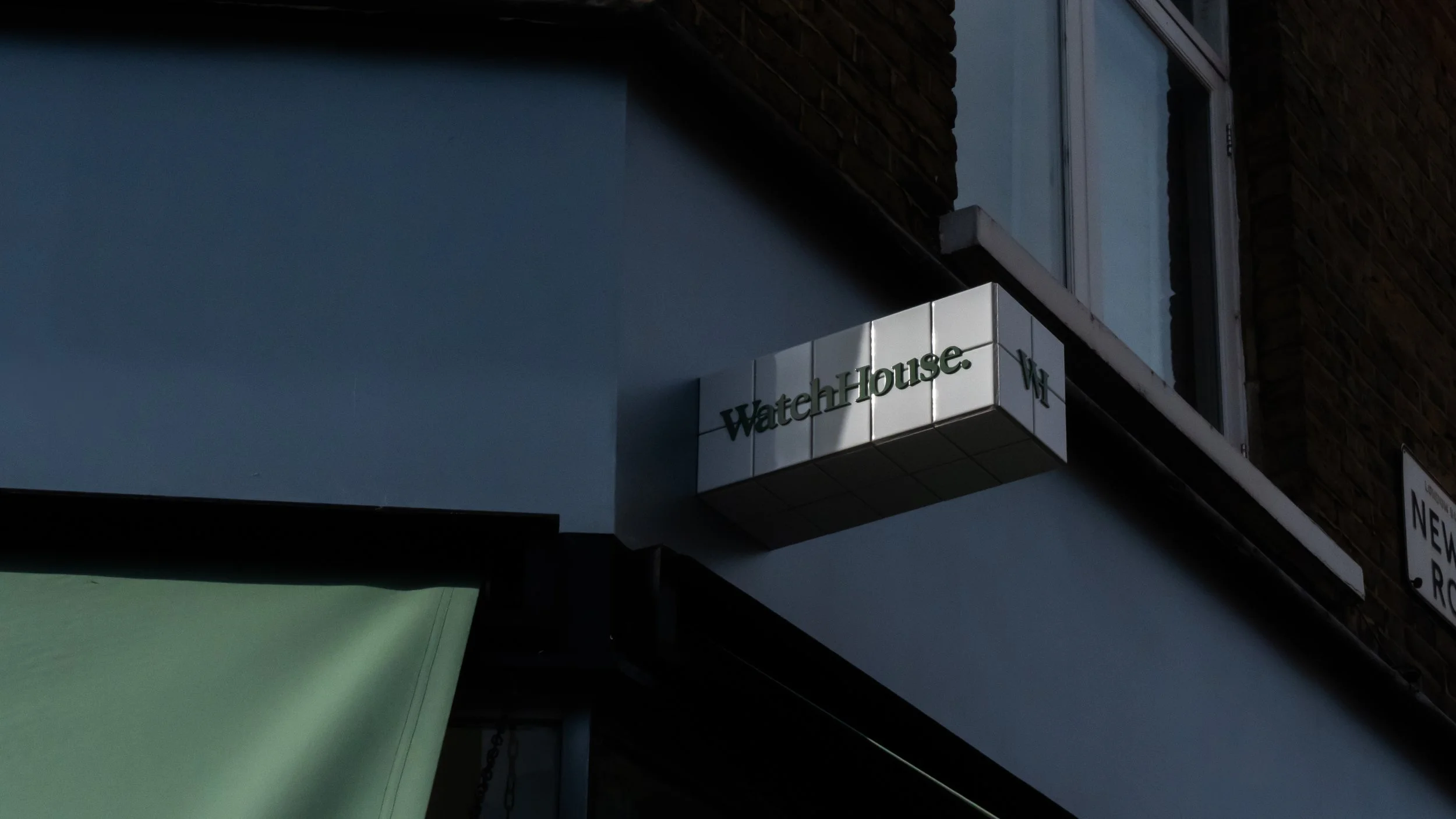 Building facade with a sign reading 'WaterhHouse' attached to the wall near a window and a green awning below.