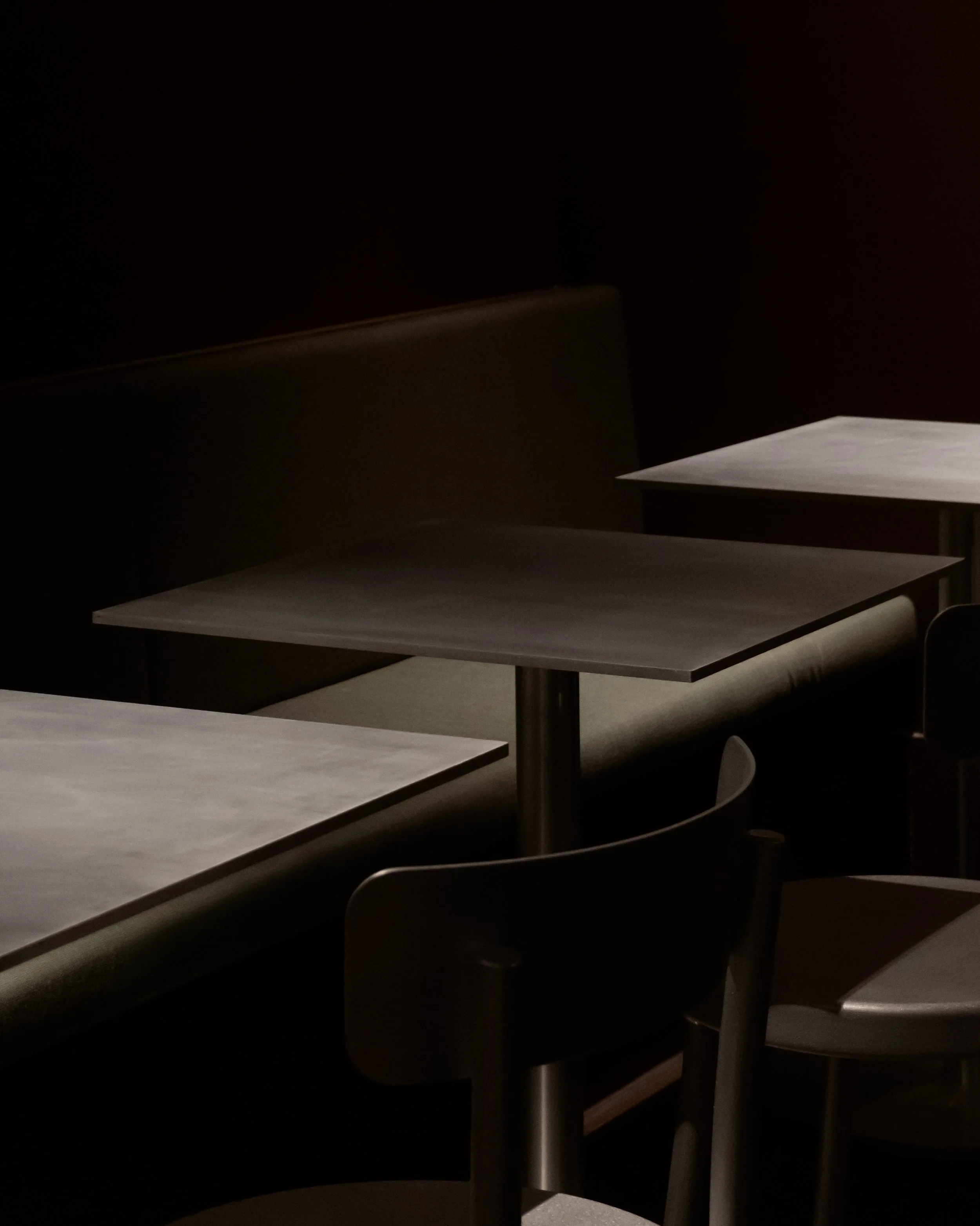 Dimly lit room with several white tables and chairs, no visible people or objects.