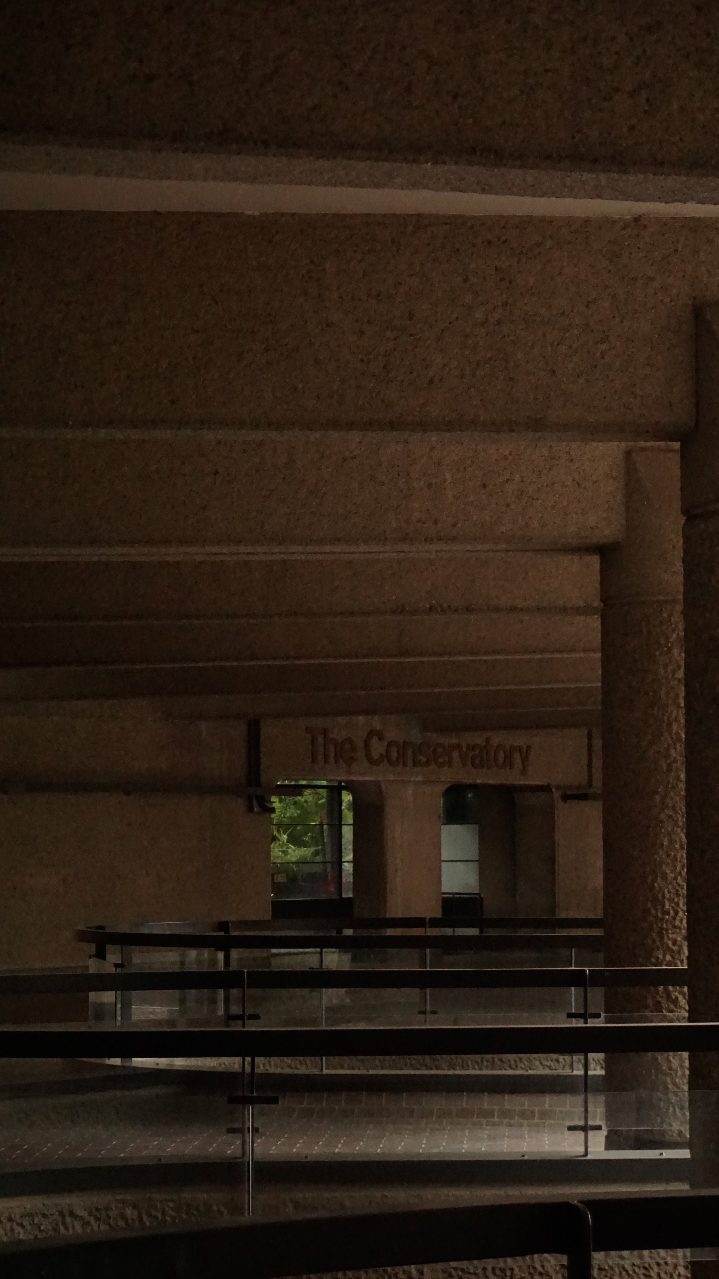 Interior view of a building with a sign that reads 'The Conservatory', showing stone pillars, glass windows, and a fenced area.
