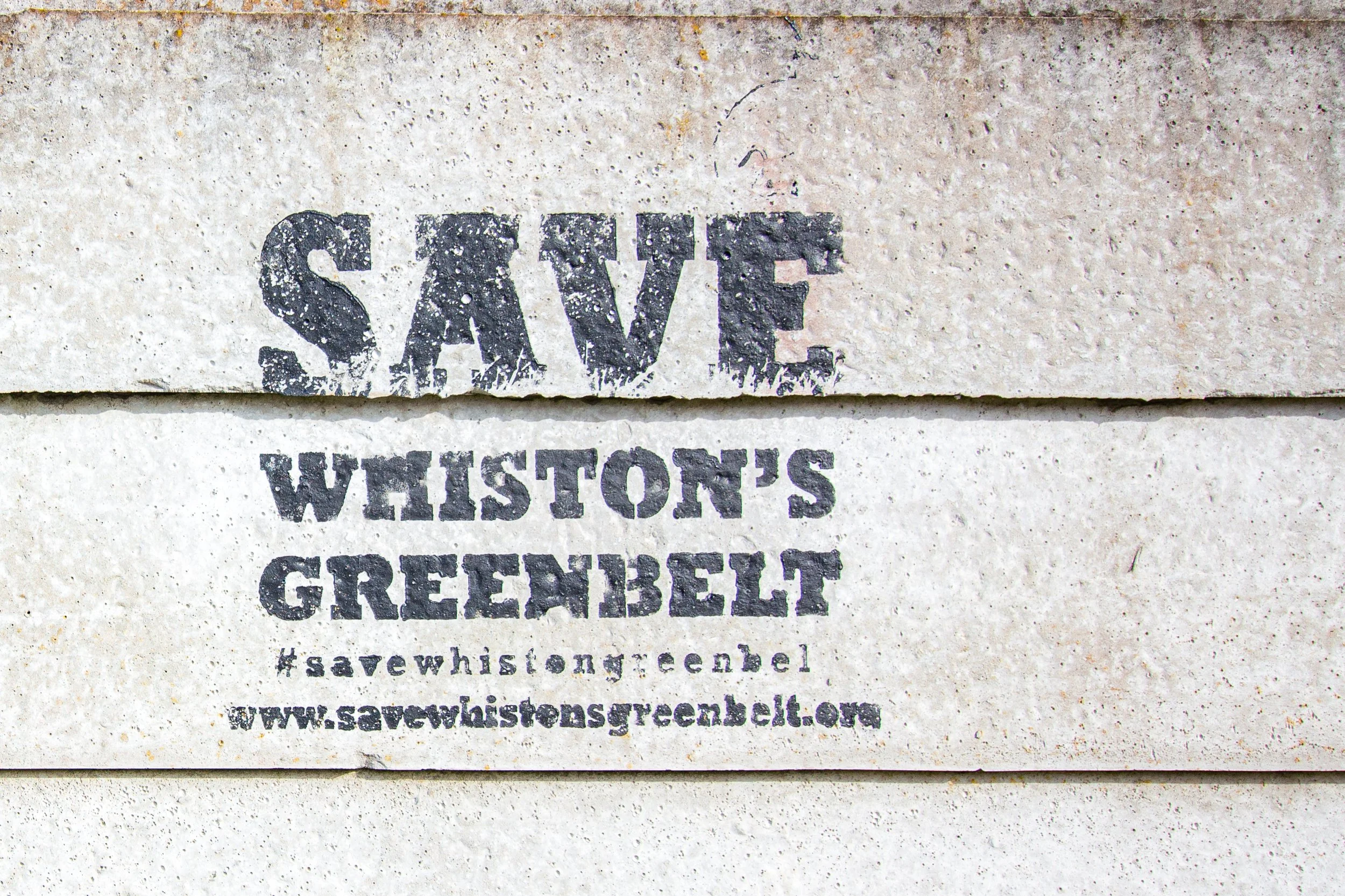 A concrete wall with a painted stencil that reads "SAVE WASHINGTON GREENBELT" and a website link at the bottom, encouraging people to save Washington's green belt land.
