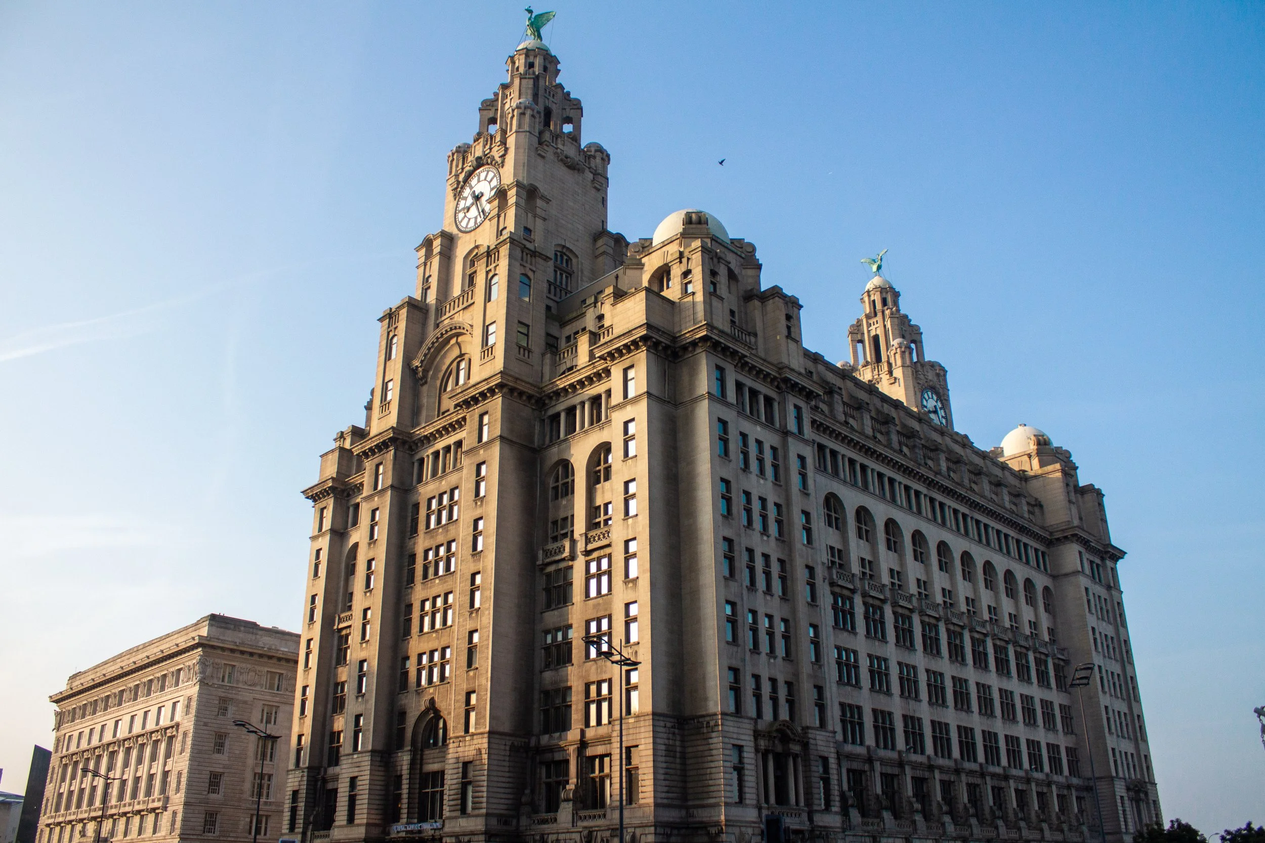 Tall historic building with clock tower and statues on top, set against a clear blue sky.