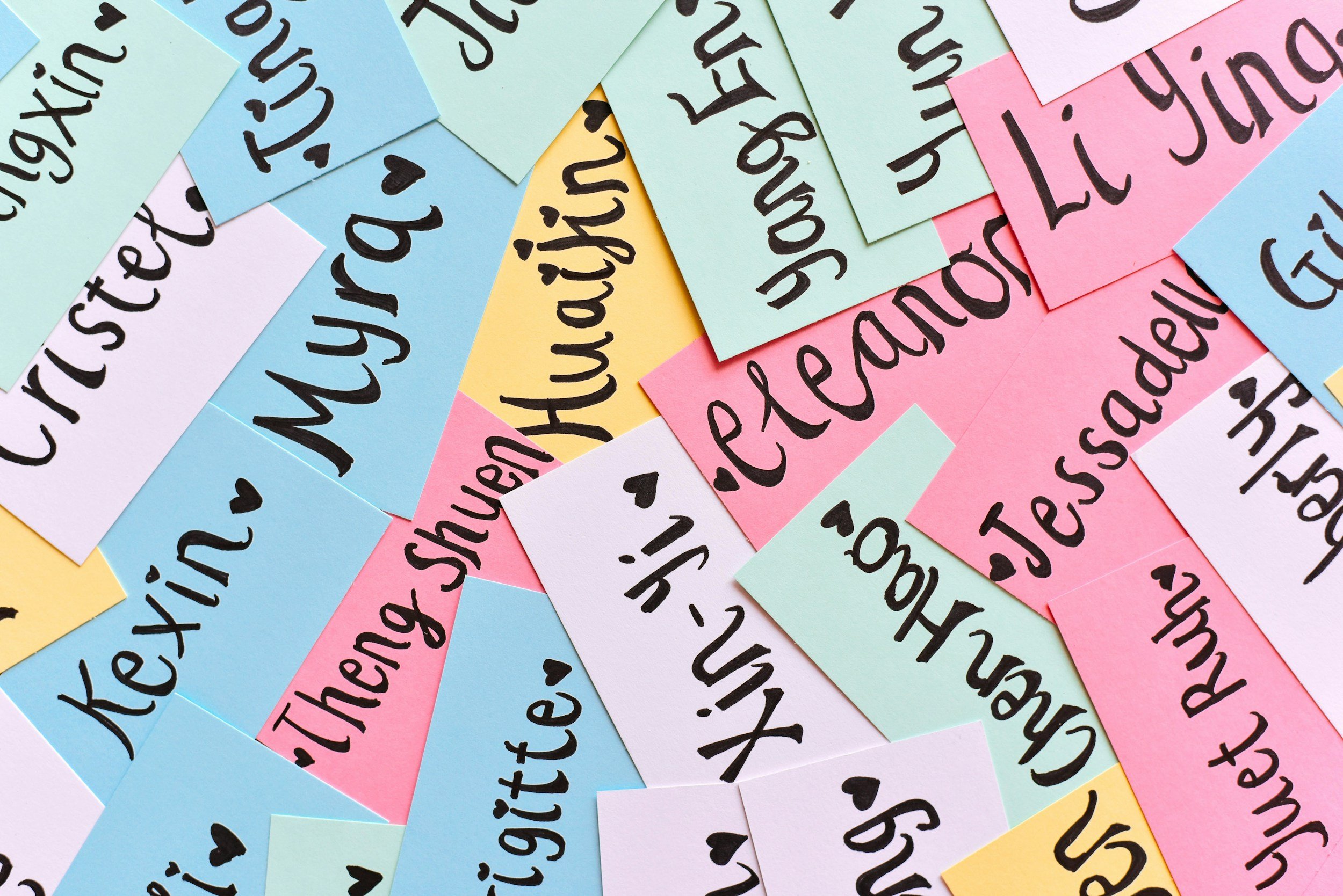 Colorful sticky notes with handwritten baby names, decorated with small black heart symbols.