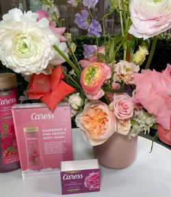 Bouquet of pink and white flowers with skincare products, including raspberry and pink pepper body wash and bar soap, displayed on a surface.