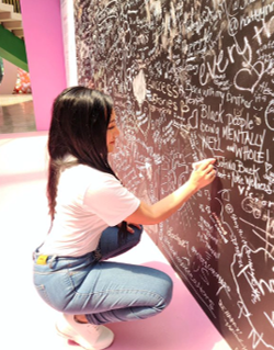 Girl writing on a chalkboard wall with various messages in a colorful room.