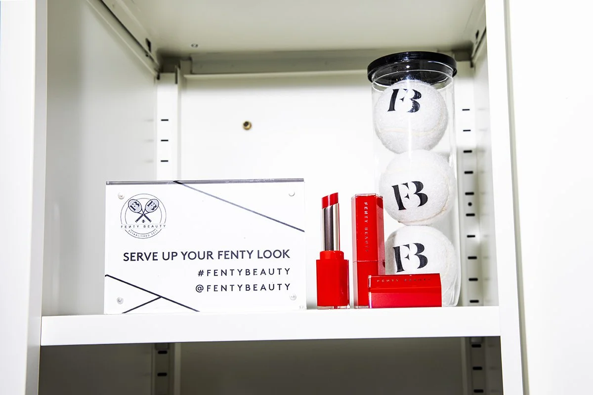 Fenty Beauty display with a sign, Fenty Beauty lipstick, and three white Fenty Beauty branded bath bombs in a clear container.