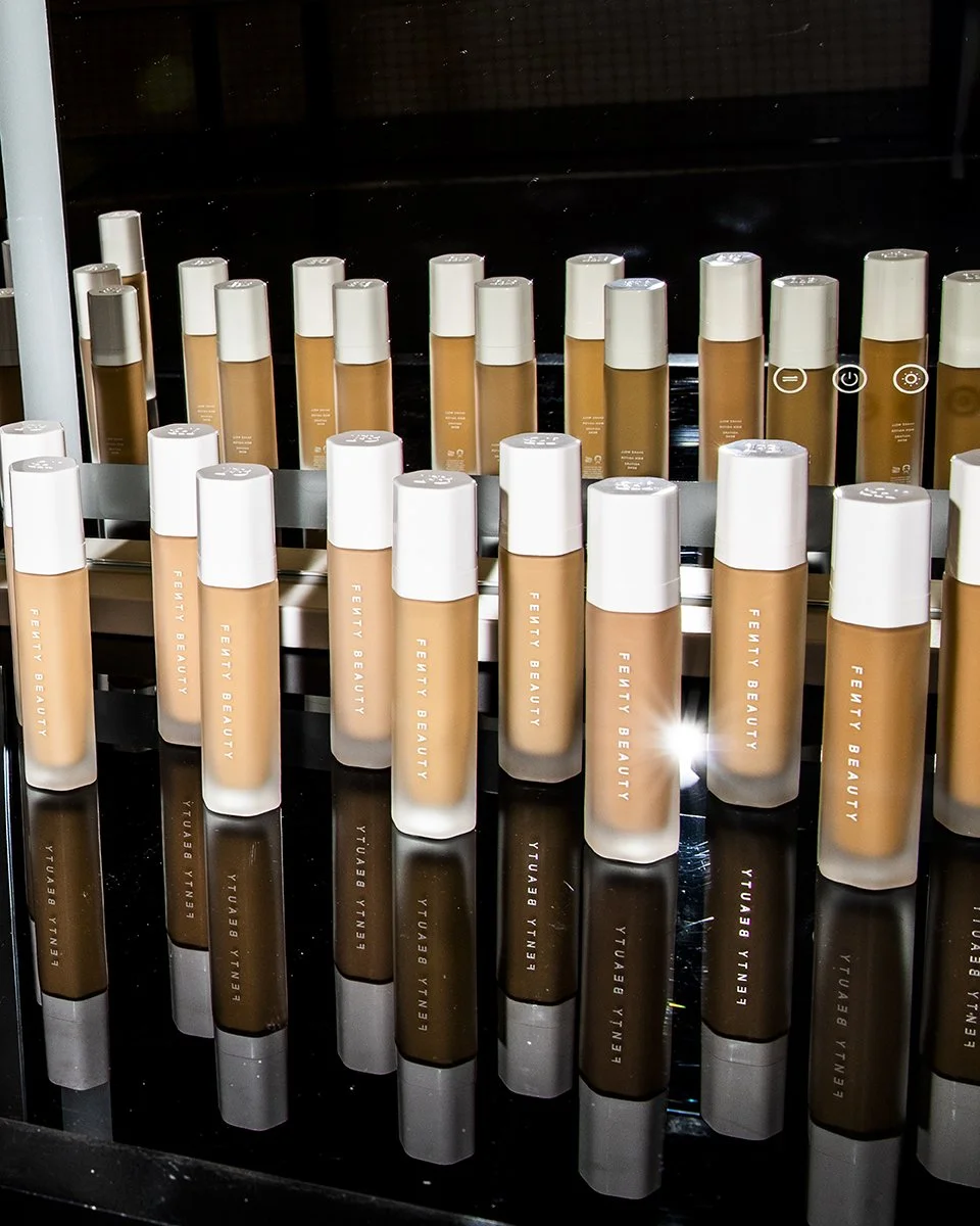 Multiple tubes of Fenty Beauty foundation arranged on a reflective black surface.