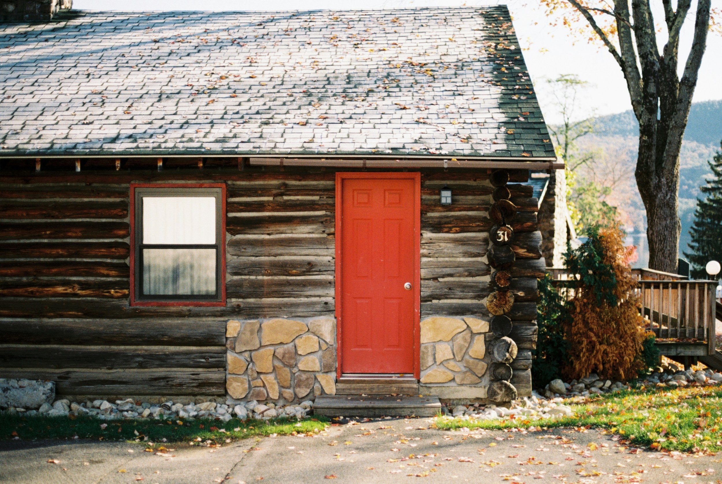 Rustic log cabin with red door and fall trees, featured in our Cabins Worth Booking guide to Boone.