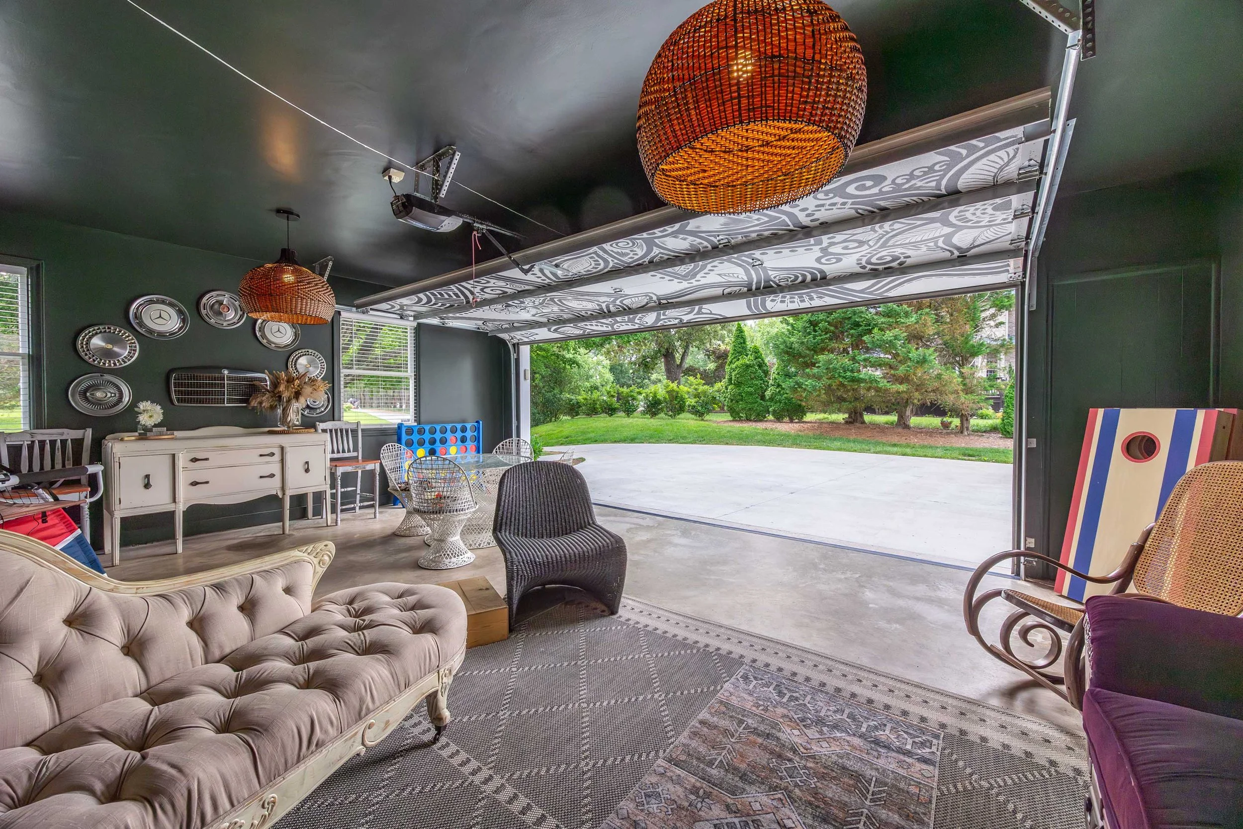 View of a cozy indoor-outdoor living space with vintage furniture, decorative wall art, and ceiling lighting, opening to a lush green yard.