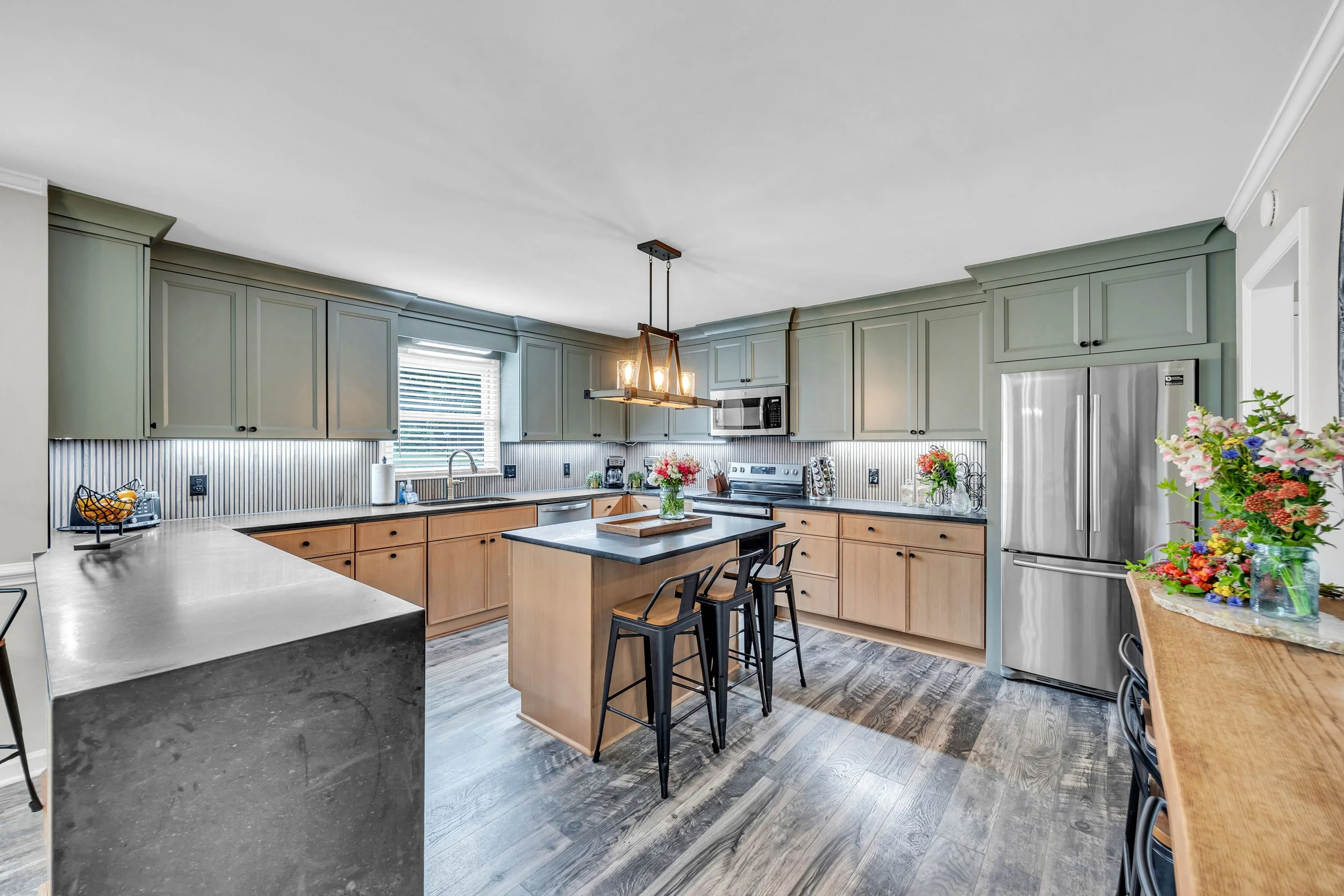Modern kitchen with green cabinetry, black and wood accents, stainless steel appliances, and decorative flowers.