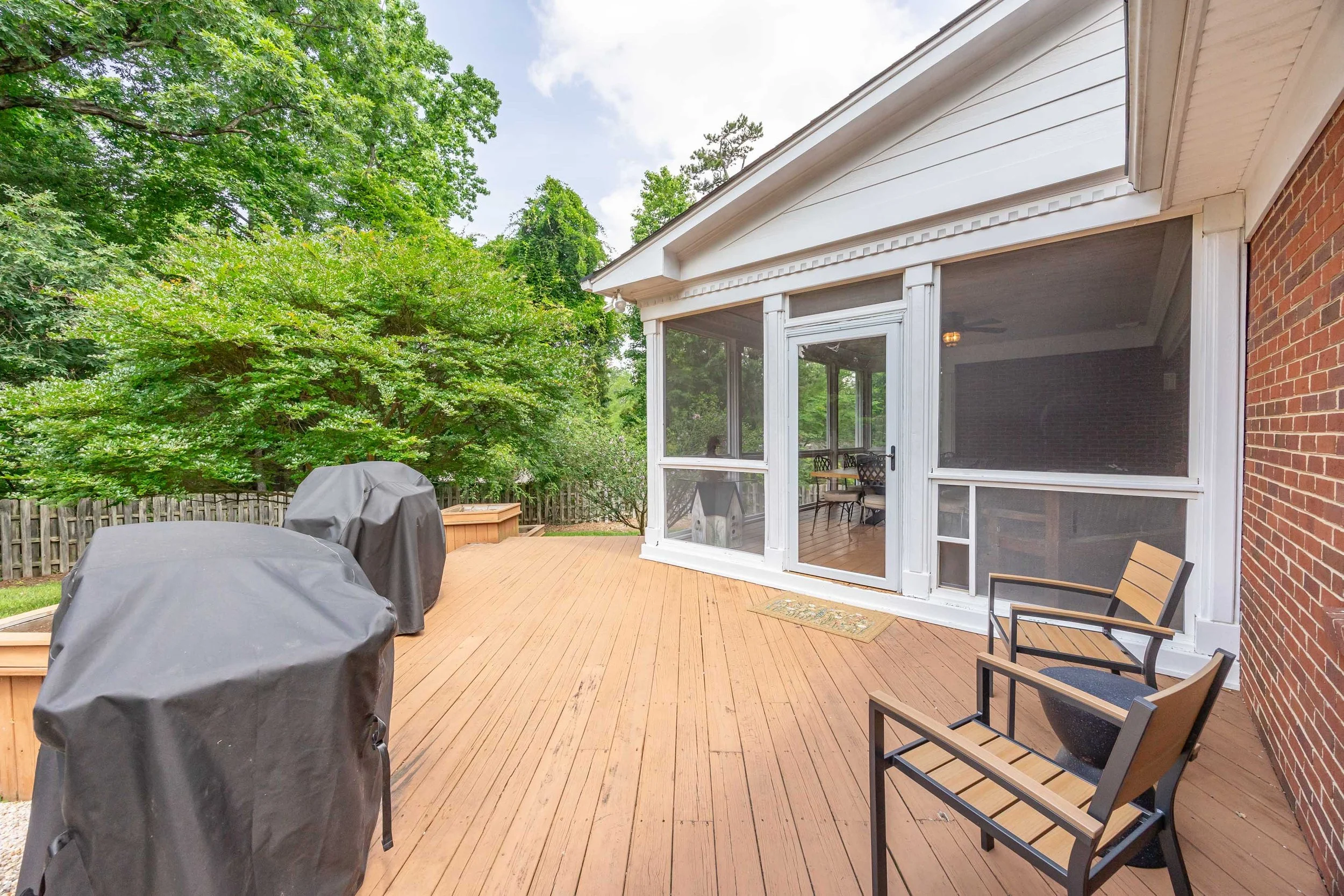 Backyard with wooden deck, covered grill, outdoor seating, brick wall, trees, and a screened porch.