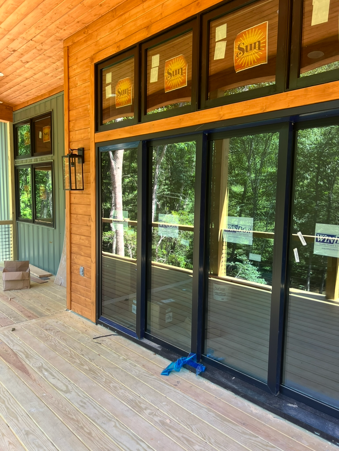 Photo of a building under construction with large glass sliding doors and windows, wood and metal siding, and a wooden deck.