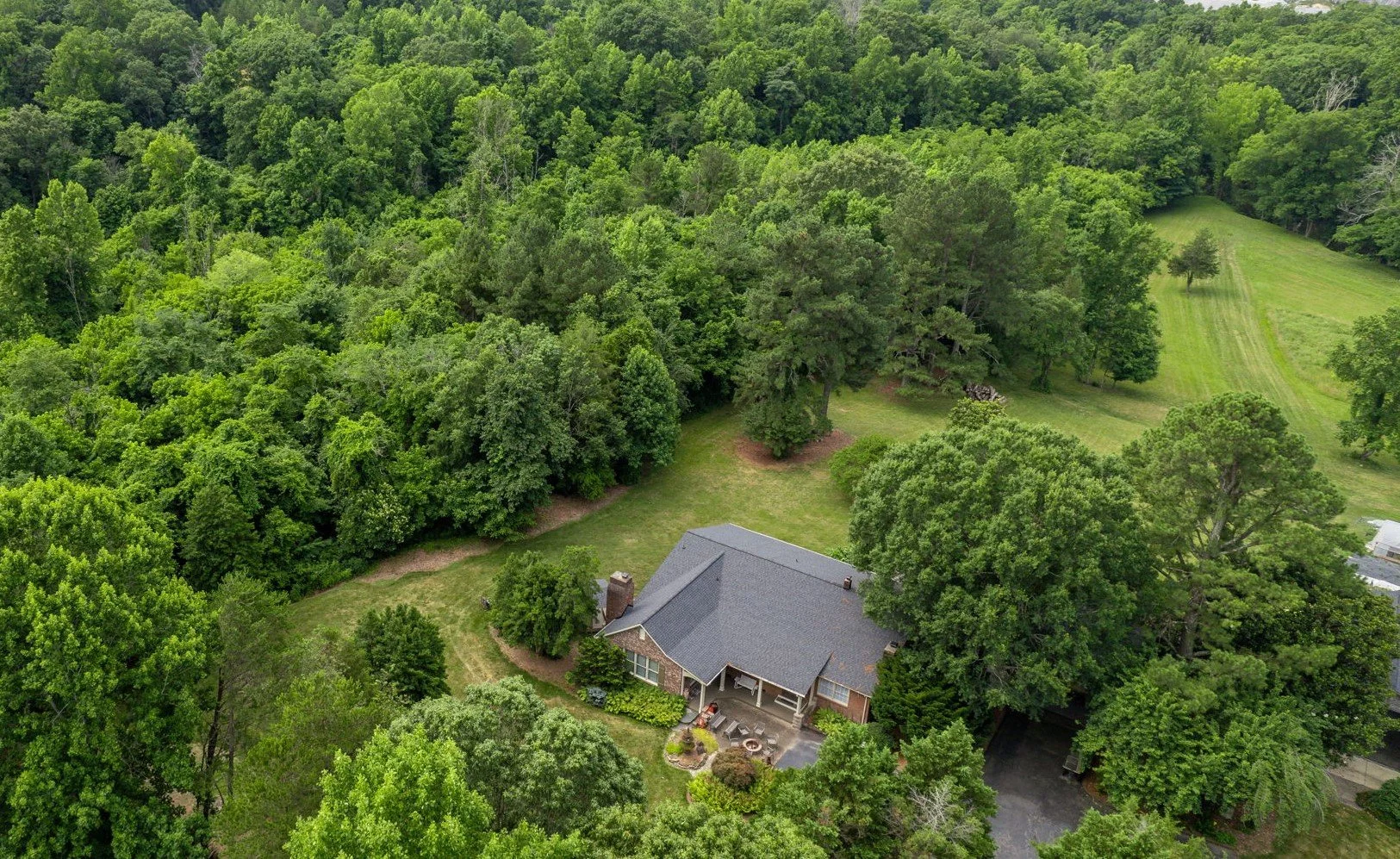 Aerial view of a house surrounded by abundant green trees and a well-maintained lawn.