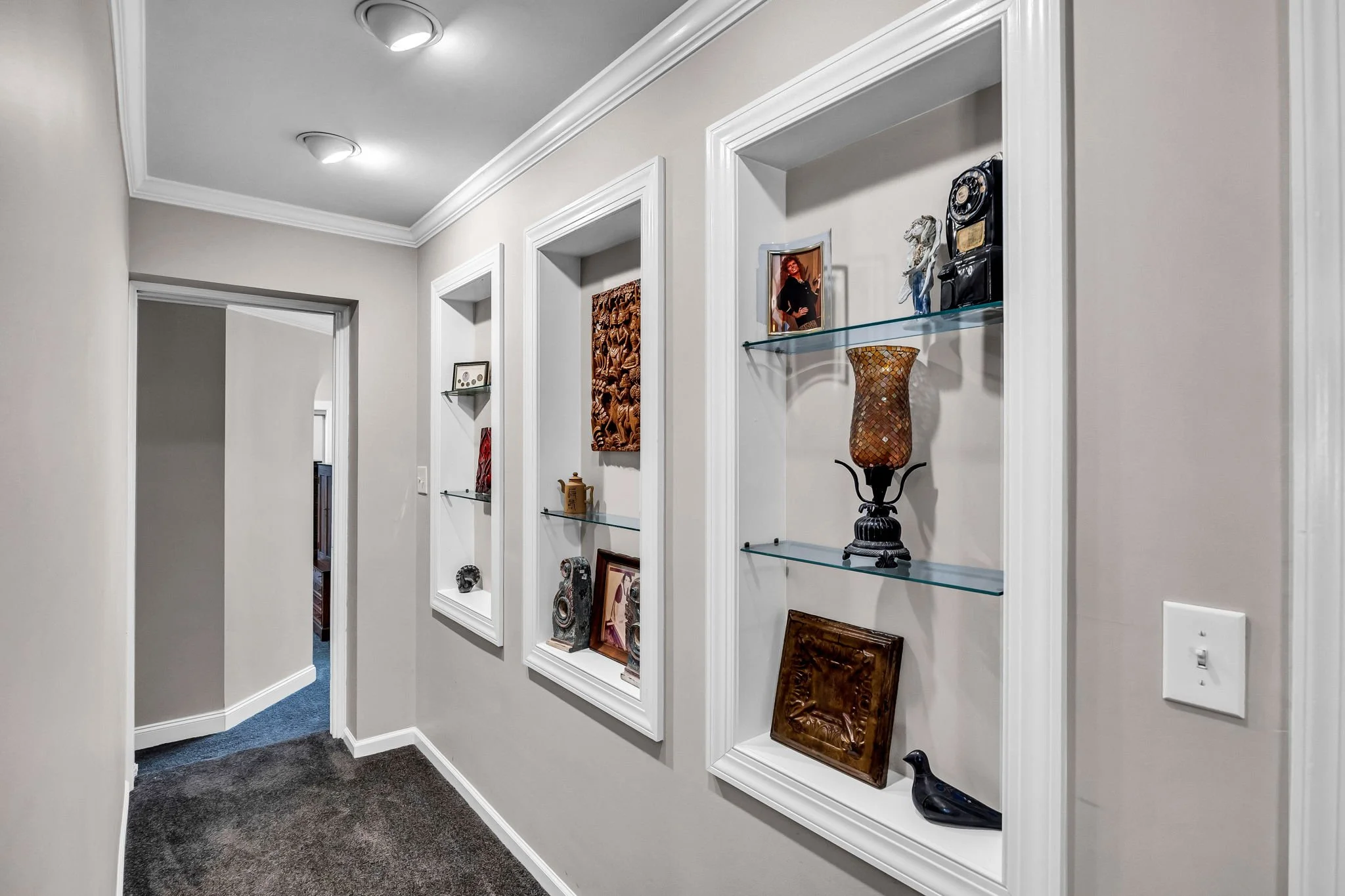 Hallway with white detailed wall molding and several decorative framed artwork and sculptures on glass shelves
