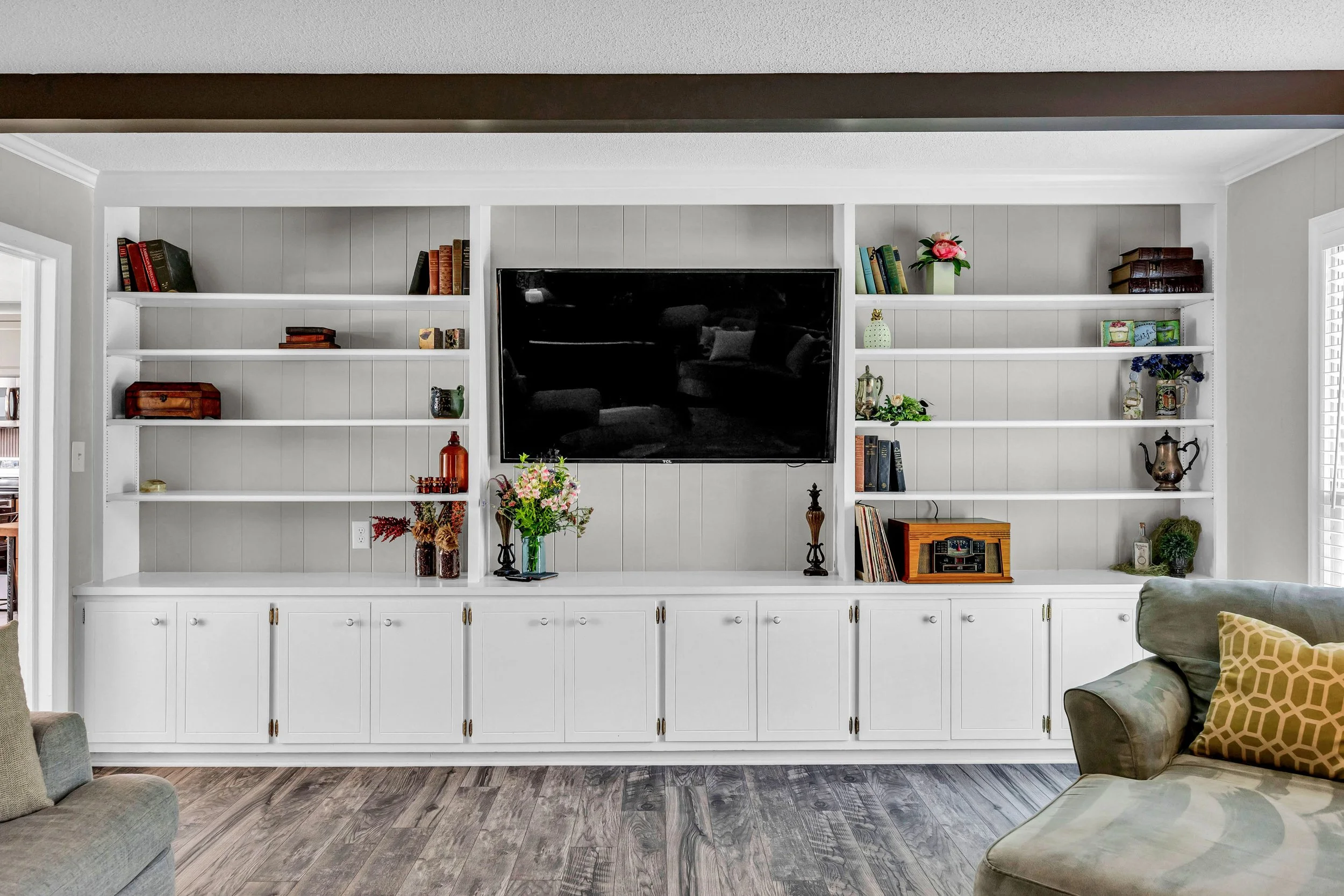 White built-in shelves with decorative books, vases, and plants, including a large TV in the center, mounted on a gray wall in a living room.