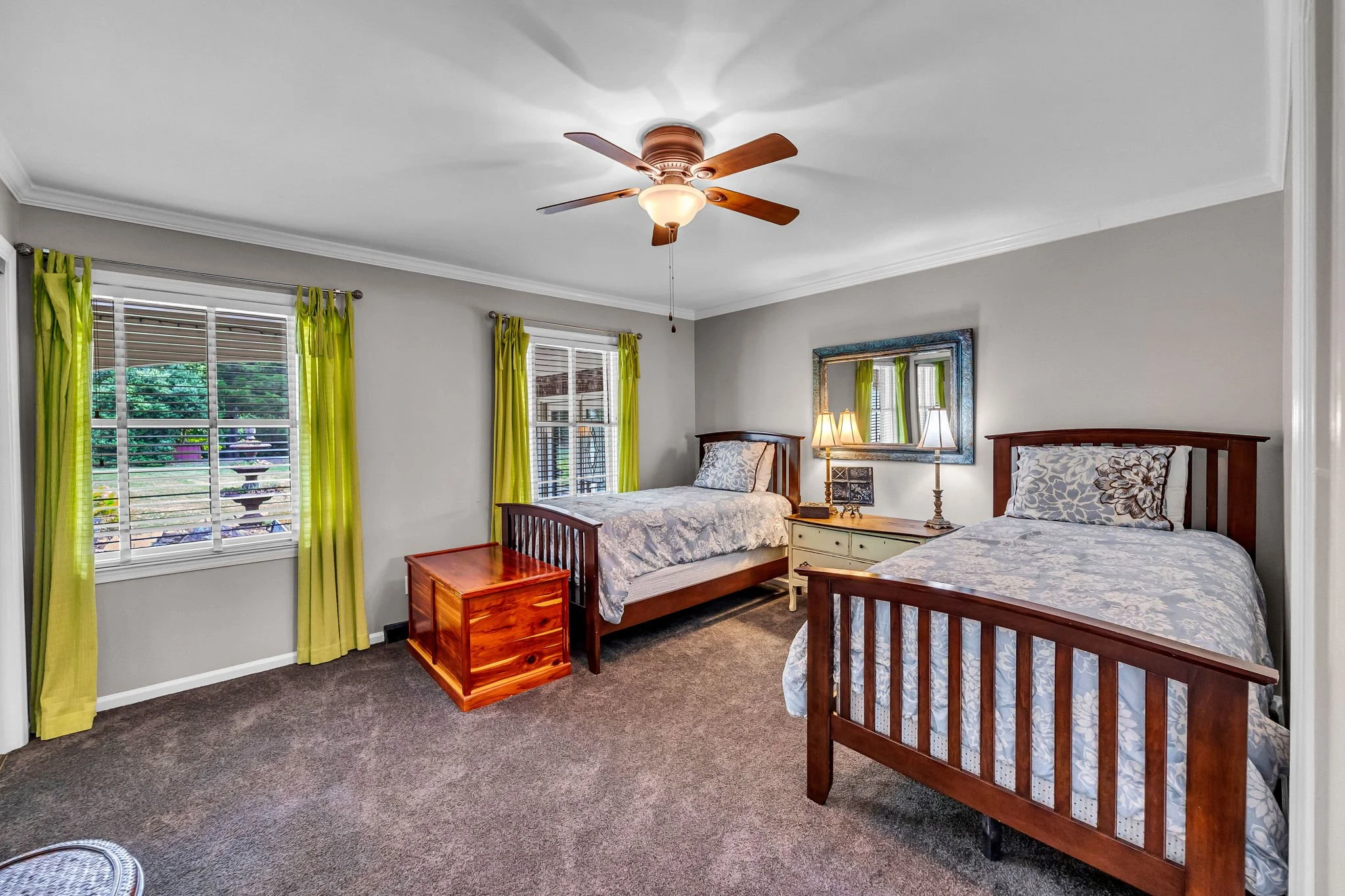 A bedroom with two twin beds, a window with green curtains, and a ceiling fan with wooden blades.