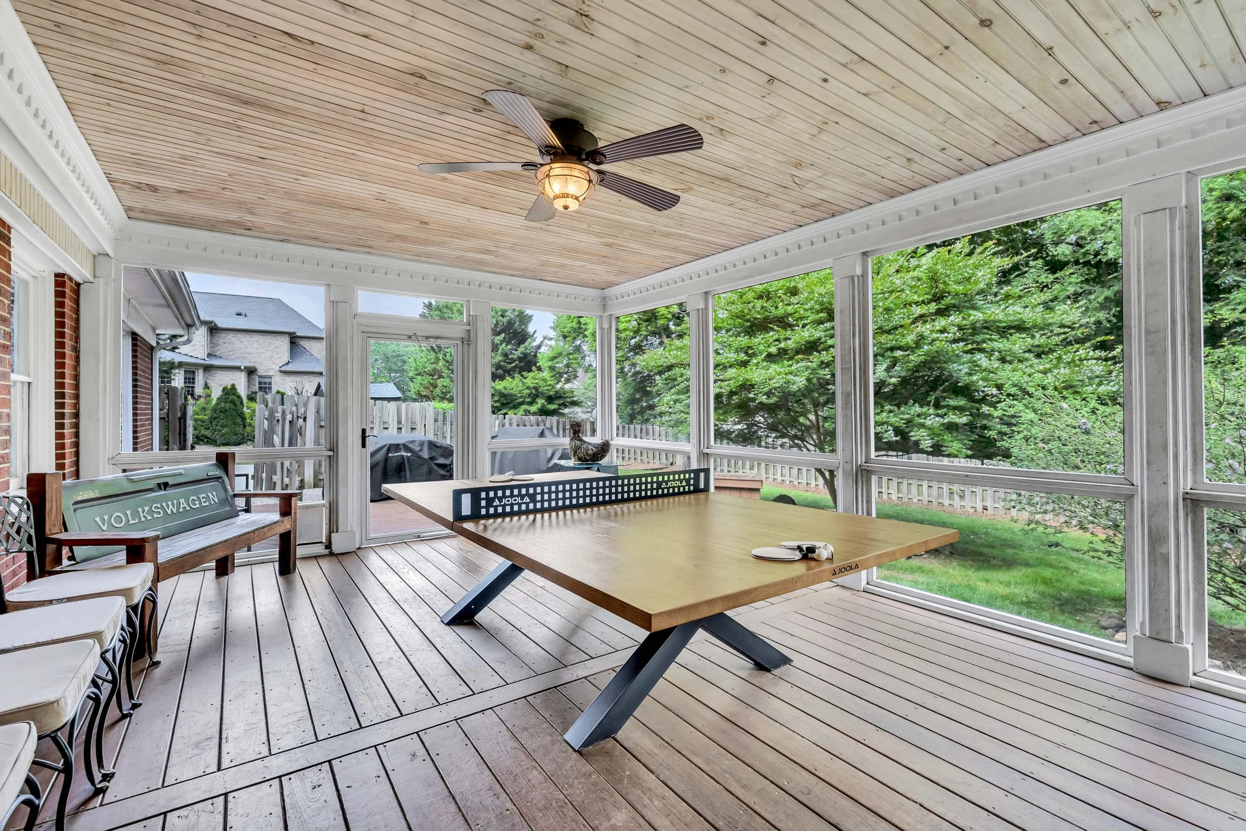 Covered porch with wooden ceiling, ceiling fan, and outdoor furniture including a table with ping pong paddles, a bench with 