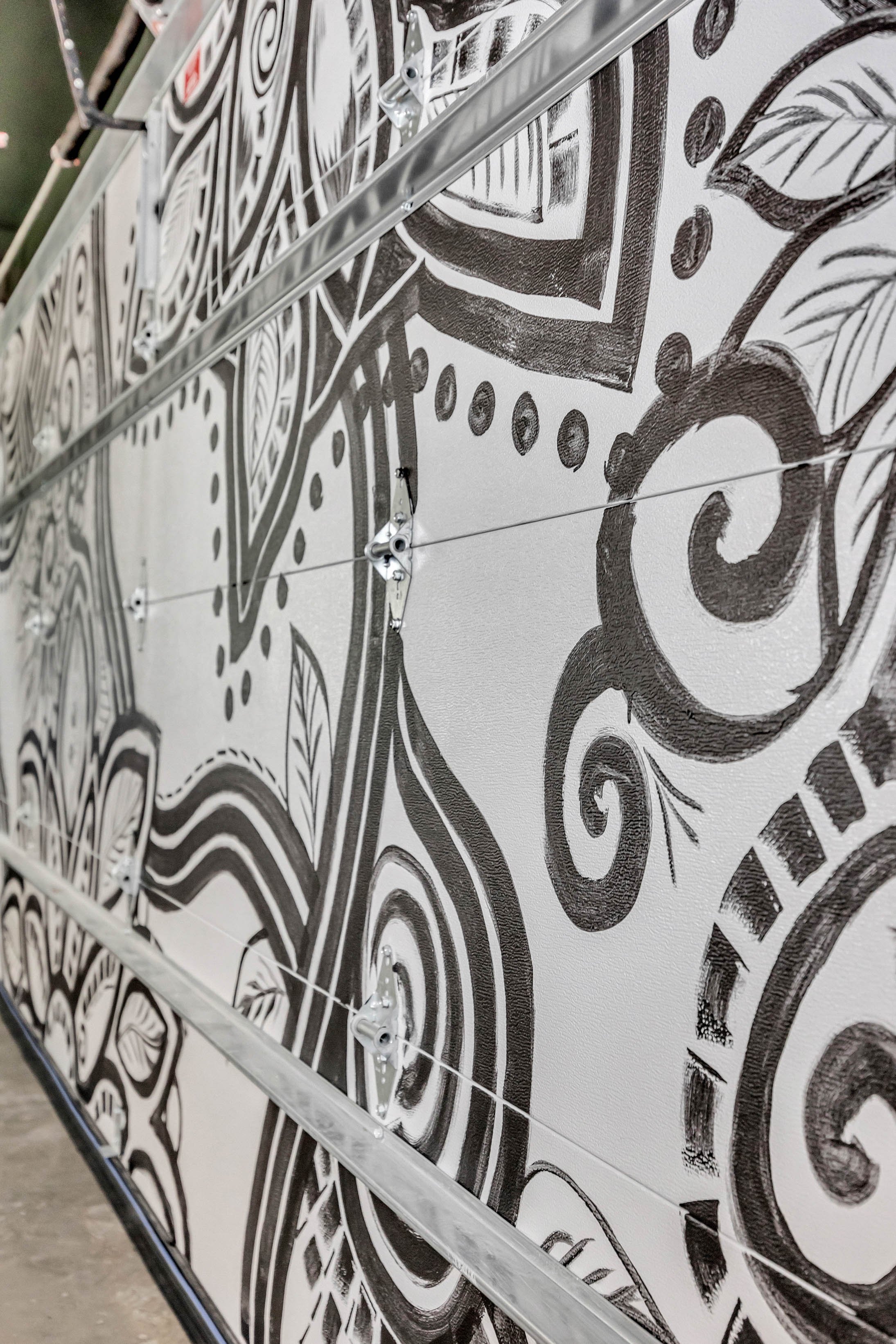 Close-up of a wall with black and white mural art featuring scrolls, leaves, and geometric shapes, with a metal frame structure in the foreground.