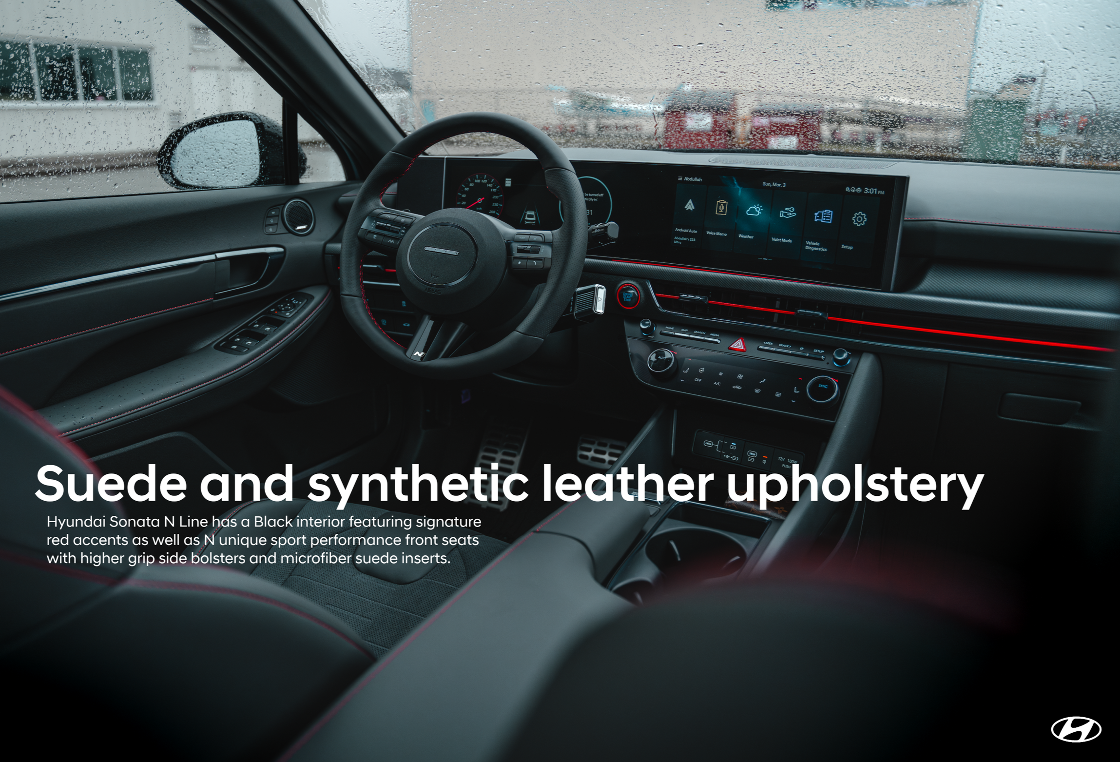 Interior view of a Hyundai Sonata N Line vehicle, showcasing a black leather and suede upholstered steering wheel and dashboard with digital screen display, raindrops on windshield, and cityscape outside on a rainy day.
