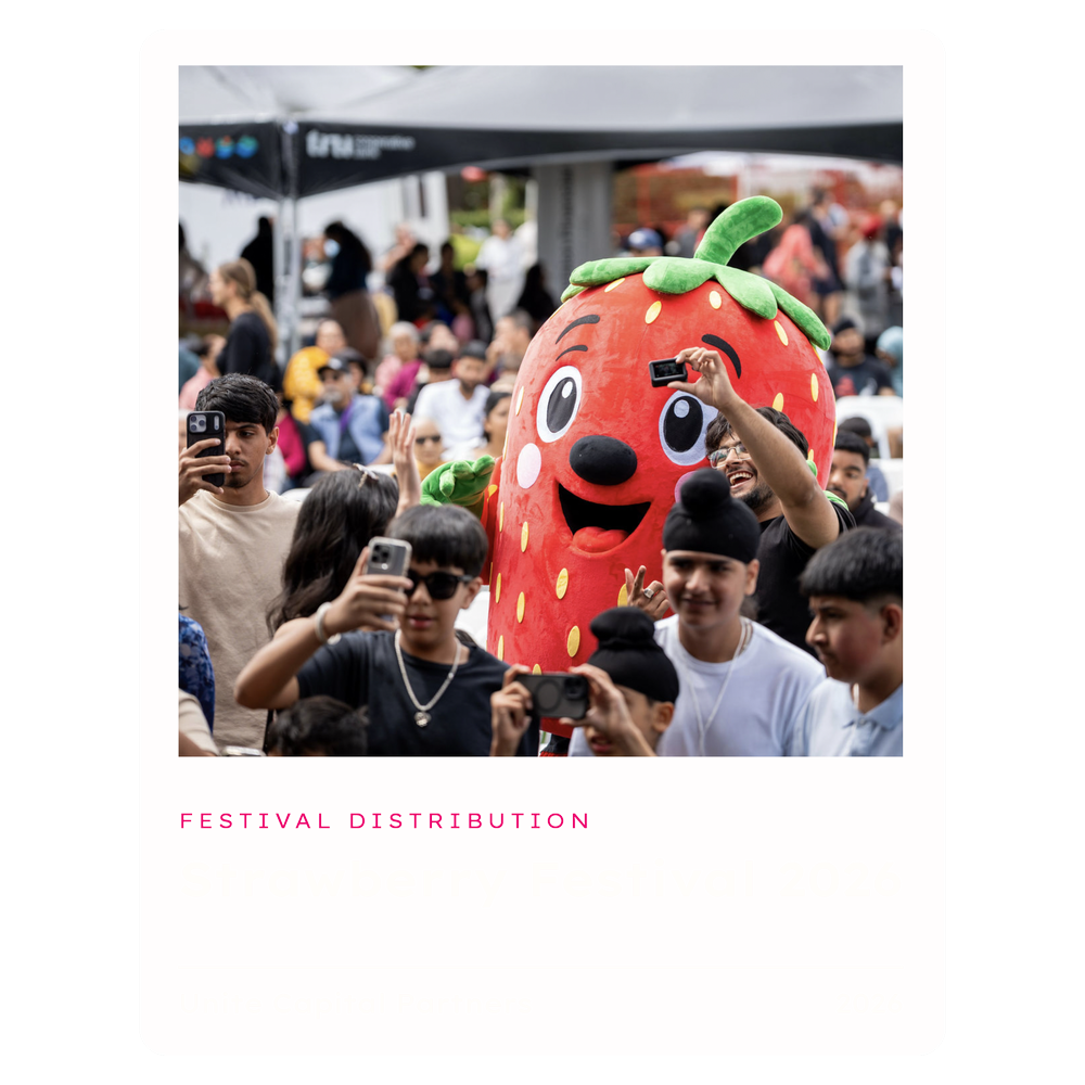 A strawberry mascot surrounded by a crowd at the Strawberry Festival.