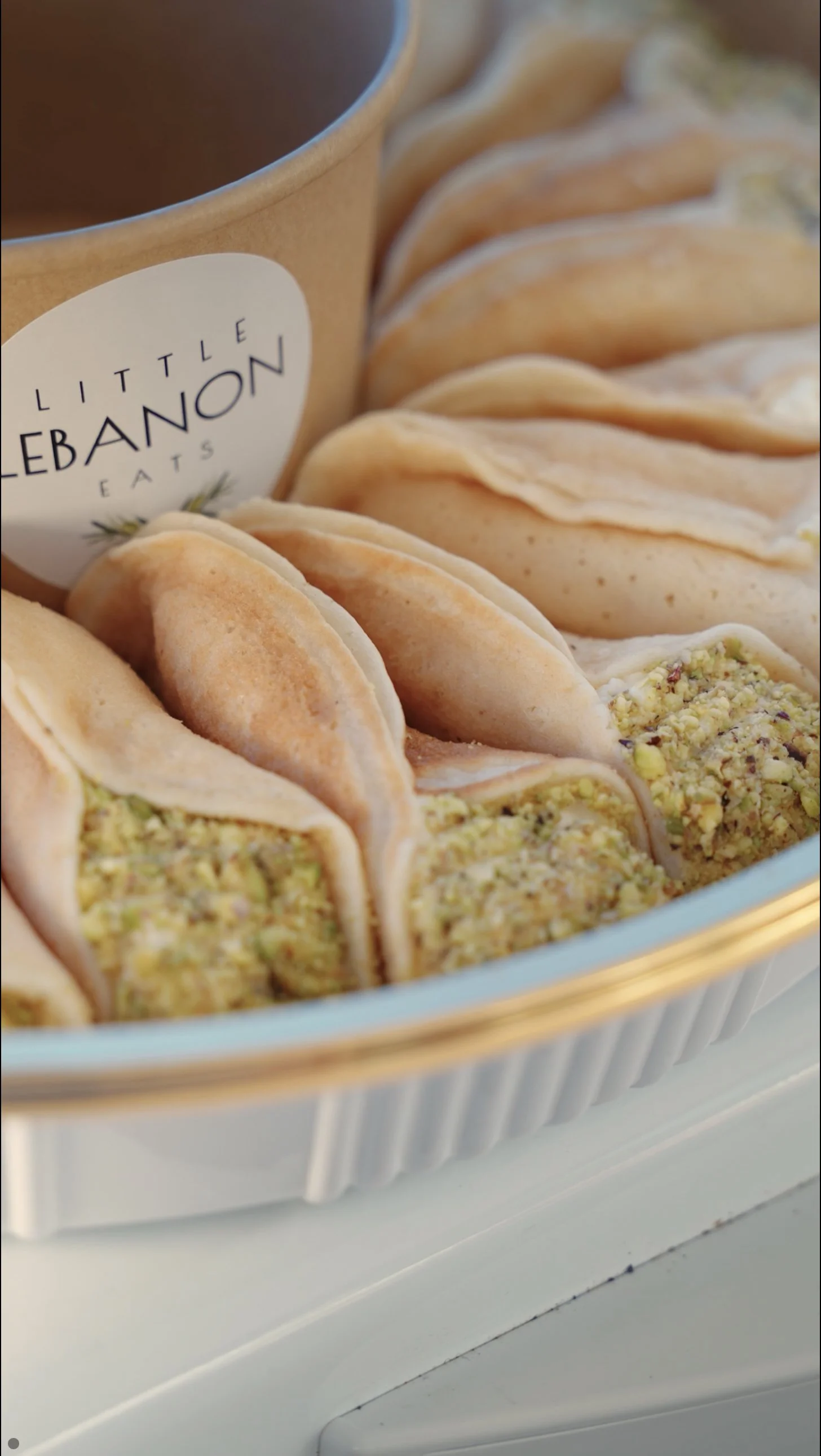 Assorted Middle Eastern desserts called baklava with chopped pistachios and a small jar labeled 'Little Lebanon Eats' in the background.