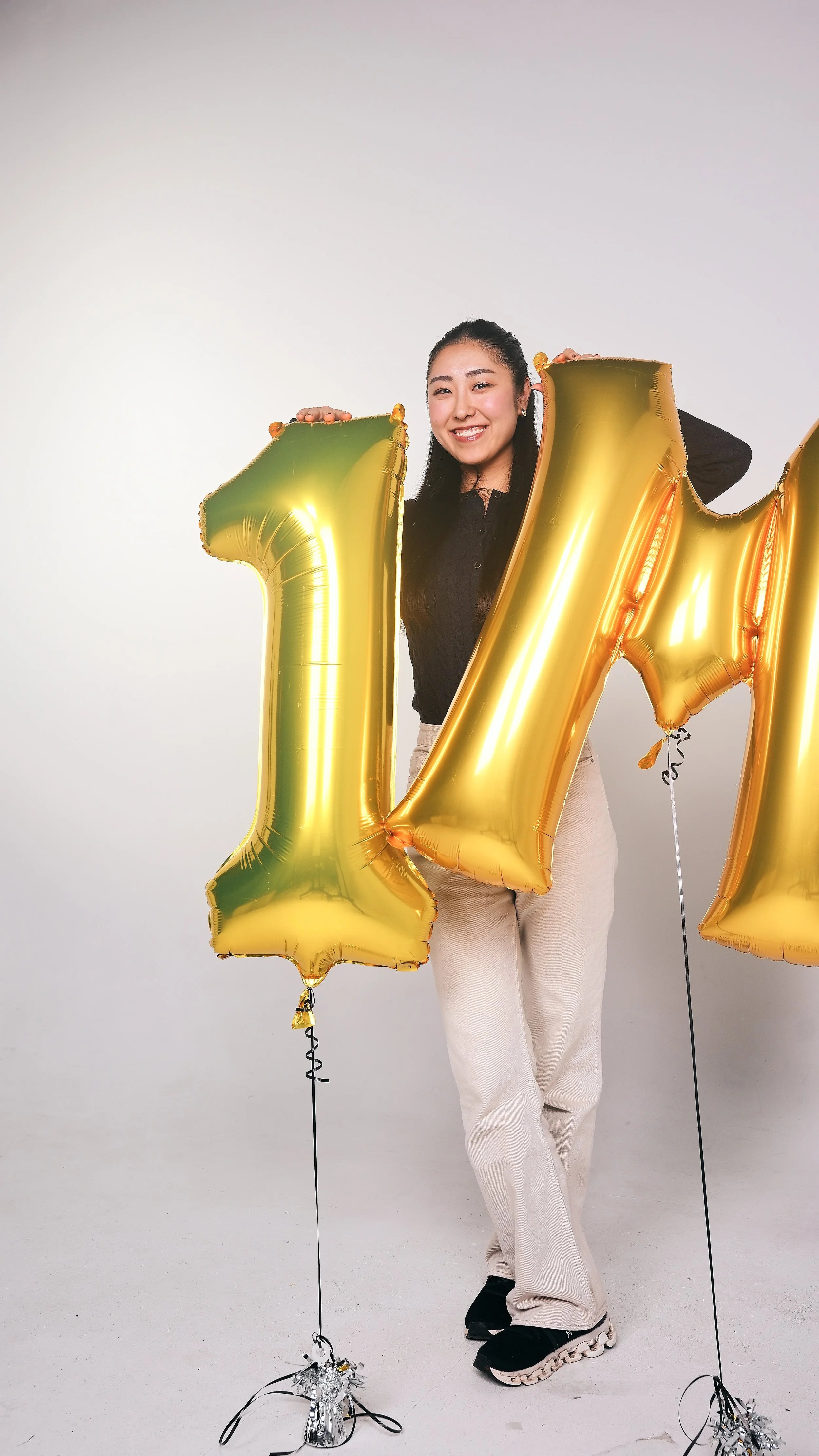 A woman smiling while holding large gold balloons shaped as the number 1 and 4, celebrating a 14th birthday or anniversary.