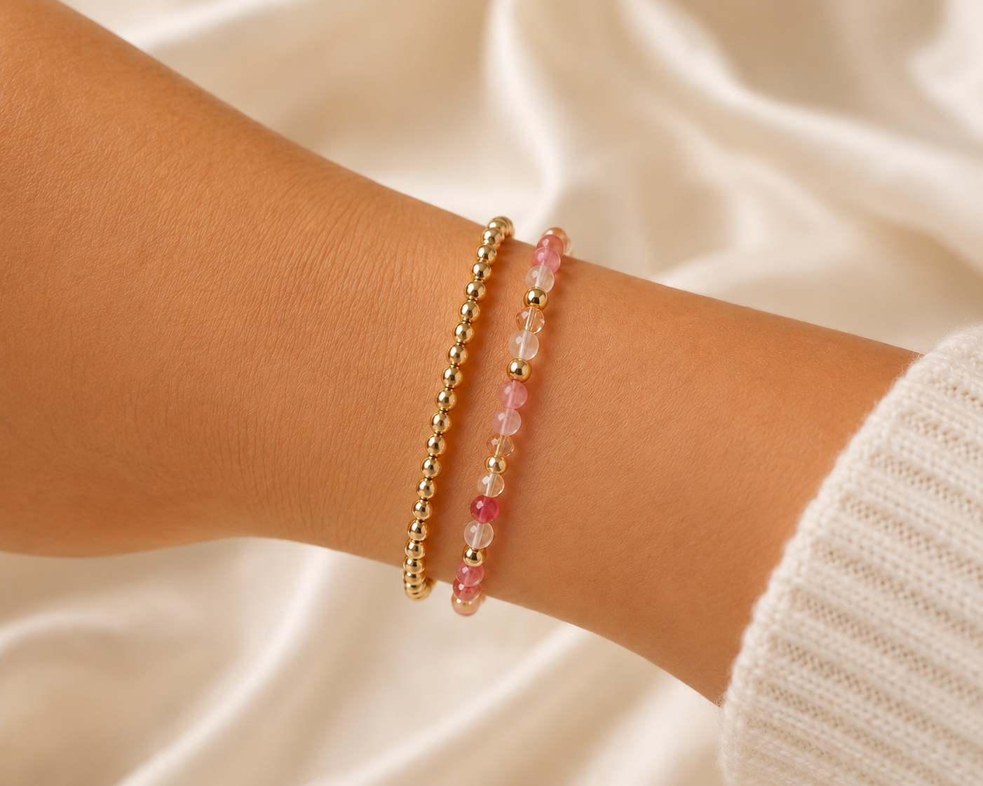 Two handcrafted RéE stretch bracelets with gold and pink beads worn on a wrist.