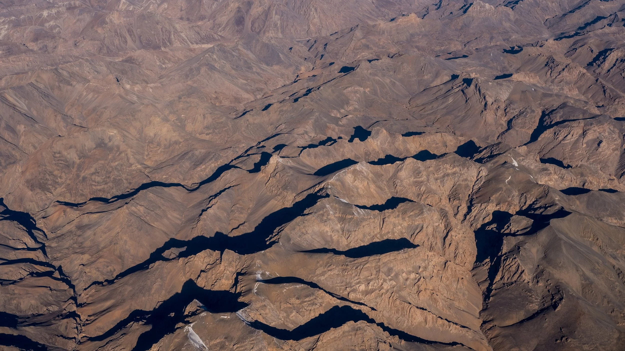 Aerial view of rugged, barren mountain terrain with deep valleys and no vegetation.