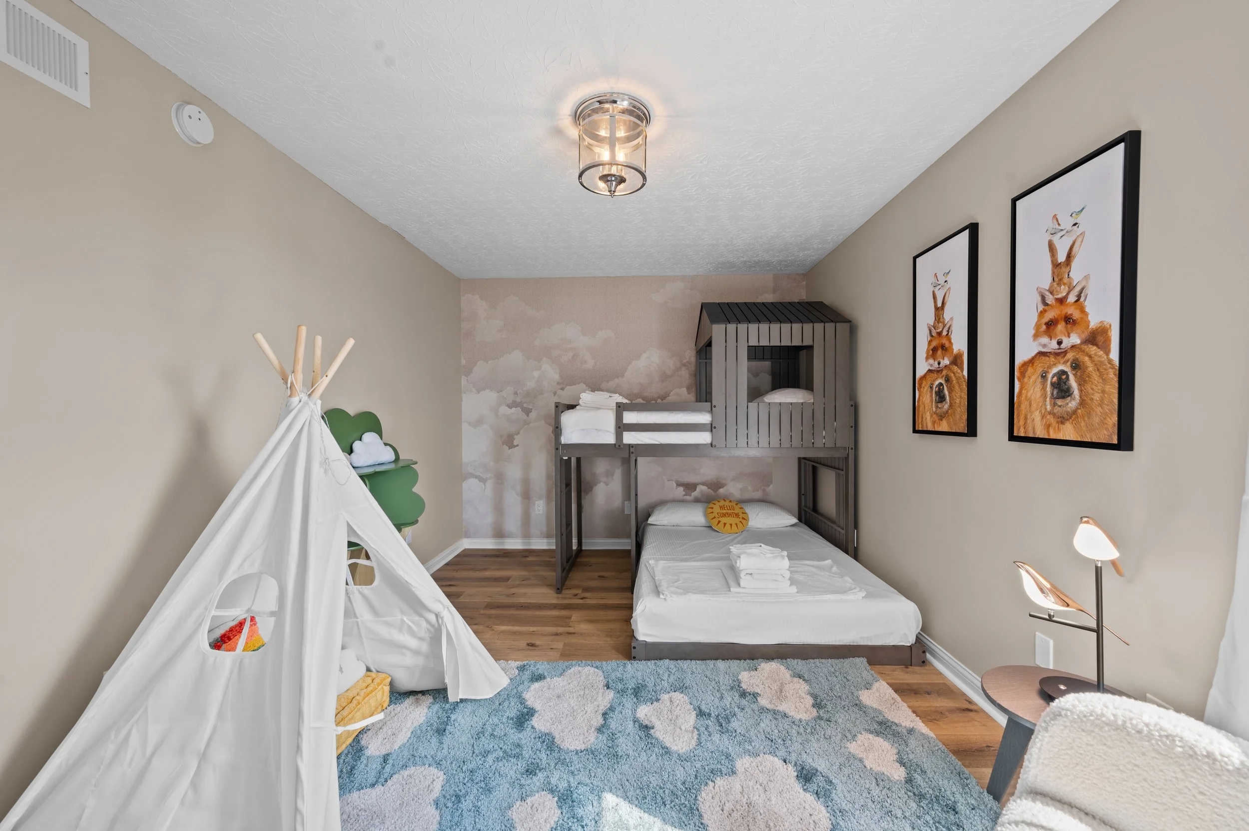 Child's bedroom with a bunk bed, a small bed, artwork featuring animals on the wall, a cozy rug, and a play tent with toys inside.