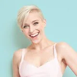 A smiling woman with short blonde hair posing against a light blue background.