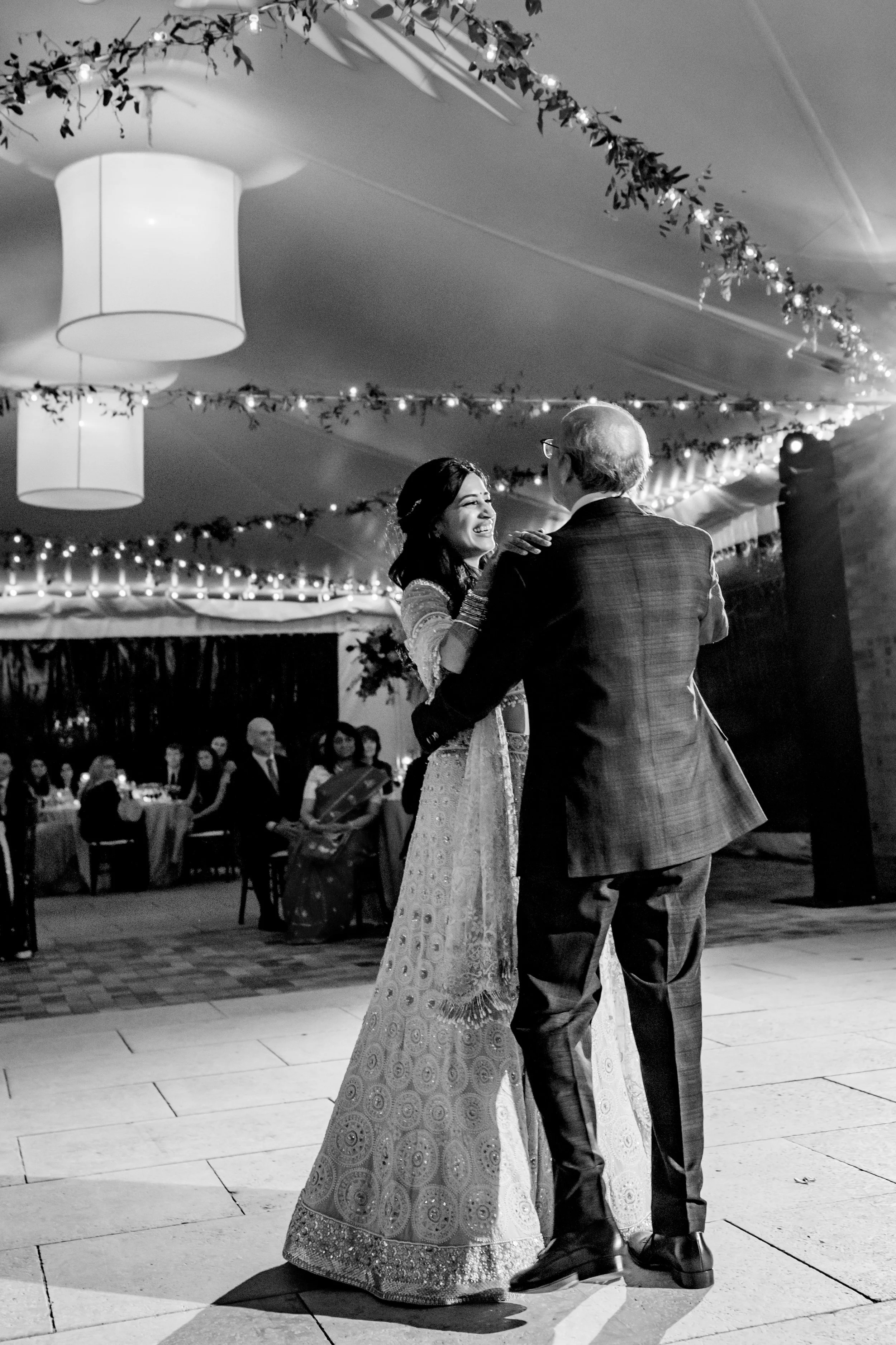 A bride and groom dancing at their wedding reception in a decorated hall, with guests seated at tables in the background.