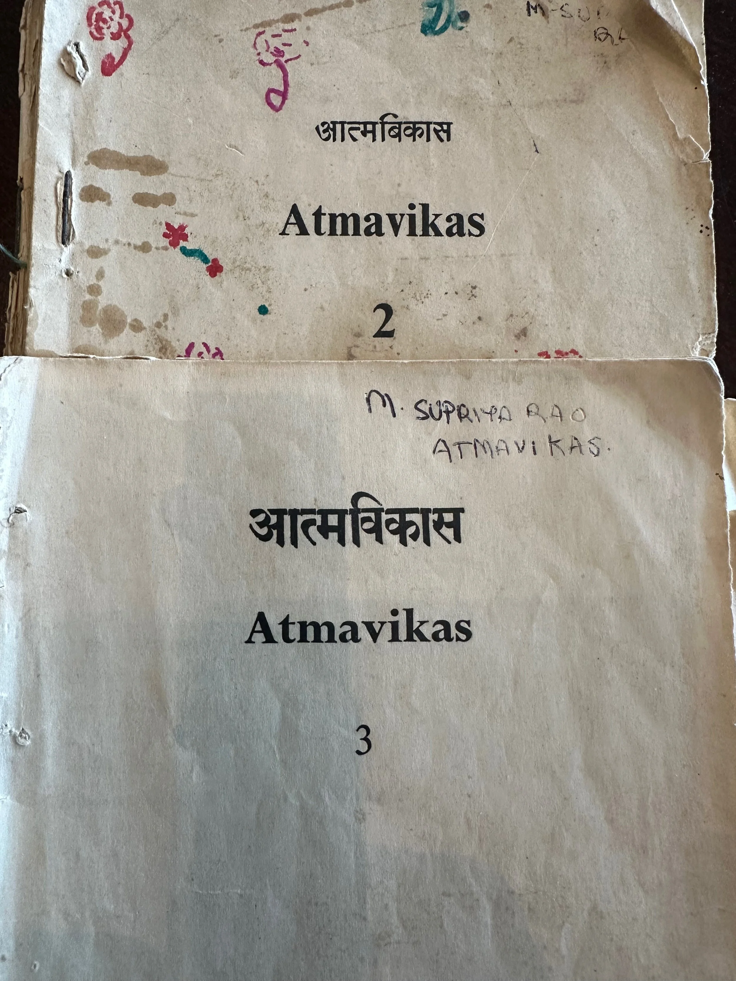 Close-up of a paper with handwritten notes and print in Hindi and English, titled 'Atmavikas', numbered 2 and 3, with colorful doodles and stains.