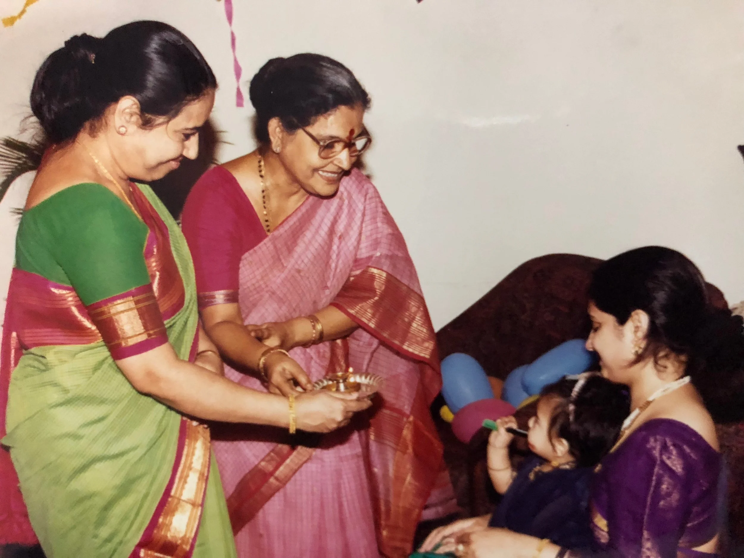 Women in traditional Indian attire celebrating Diwali, offering prayers and gifts to children.