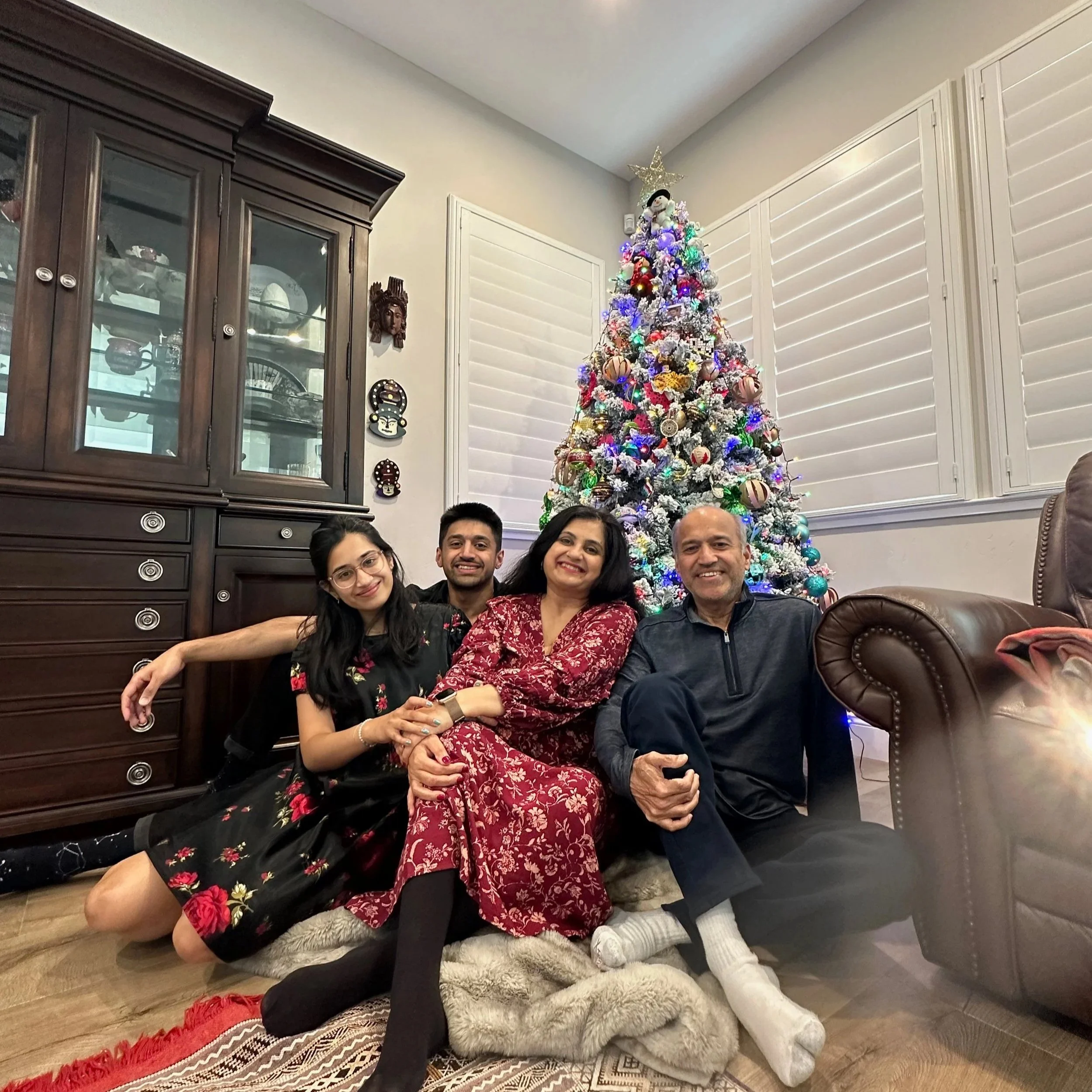 Family of four posing in front of a decorated Christmas tree in a cozy living room.