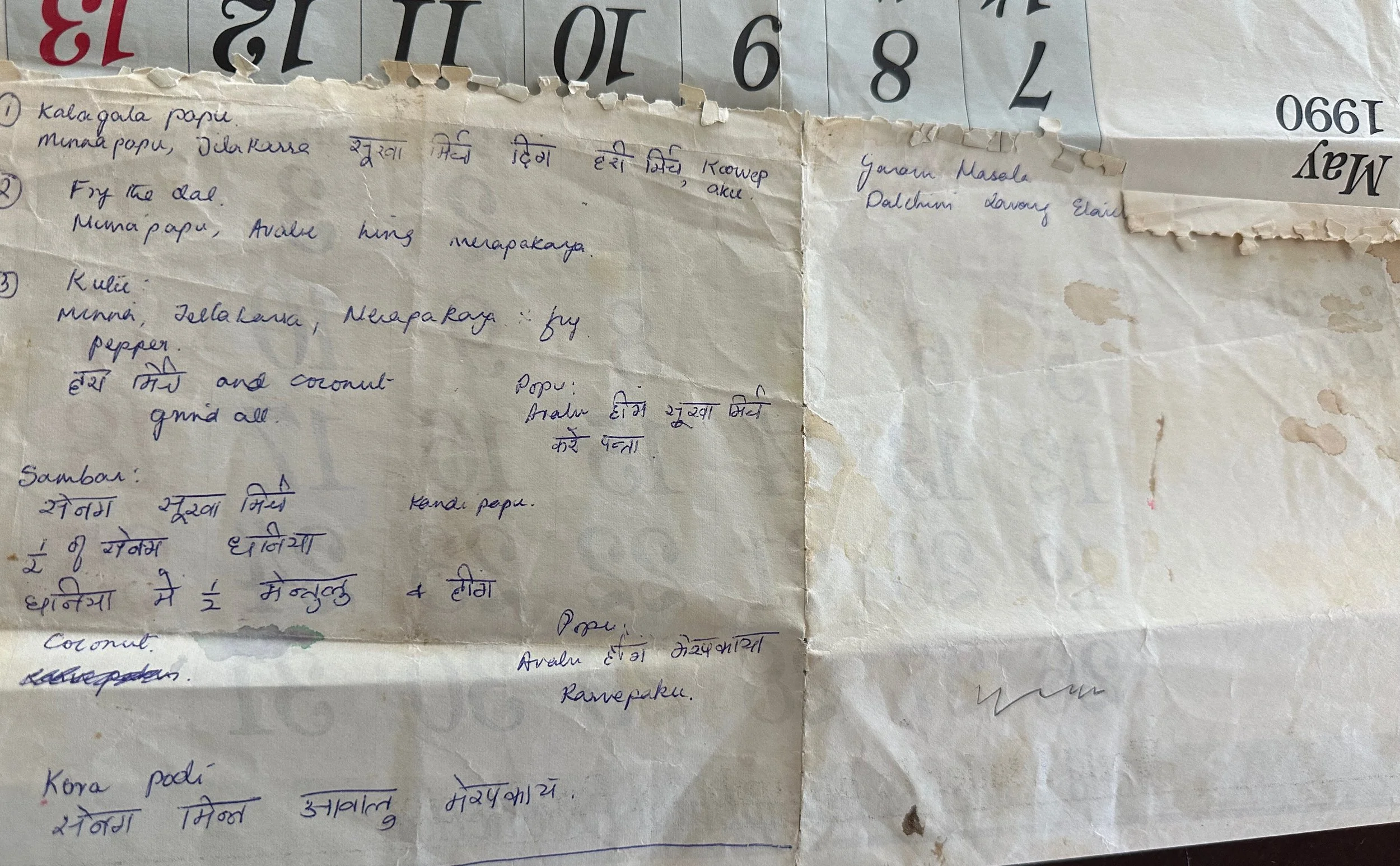 A torn piece of paper with handwritten notes in different scripts, possibly in Hindi or Nepali, placed on top of a calendar with large printed numbers.