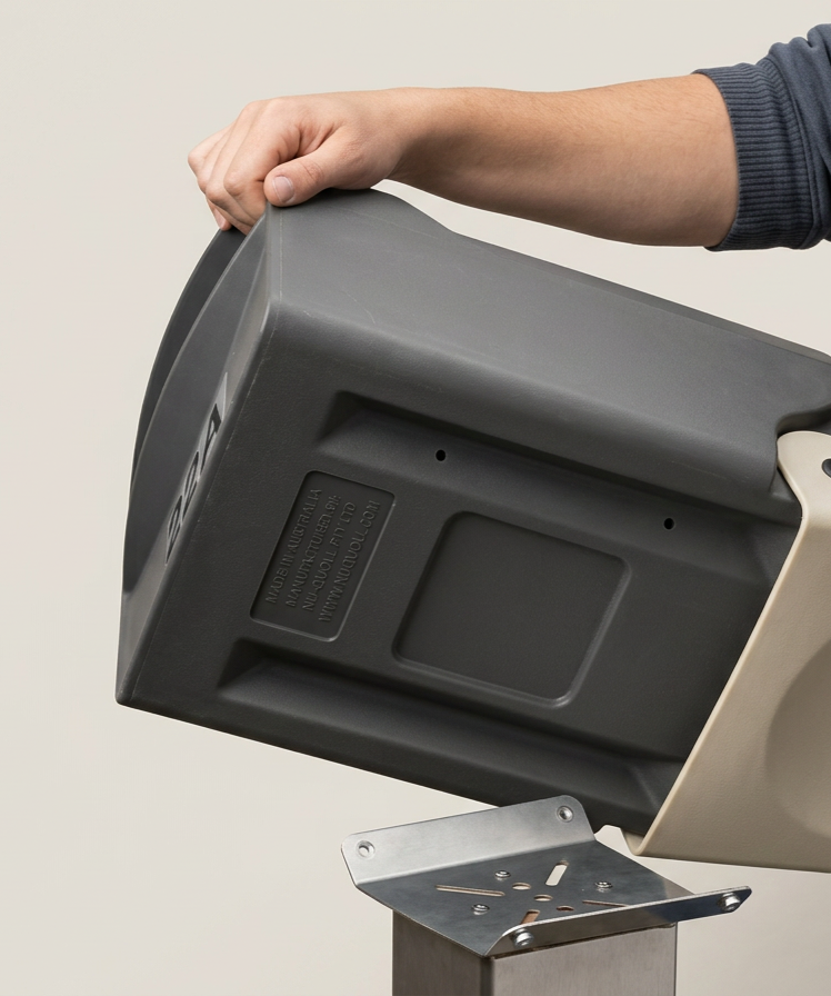A person holding a black and grey letterbox, attaching it to a metal mounting bracket.