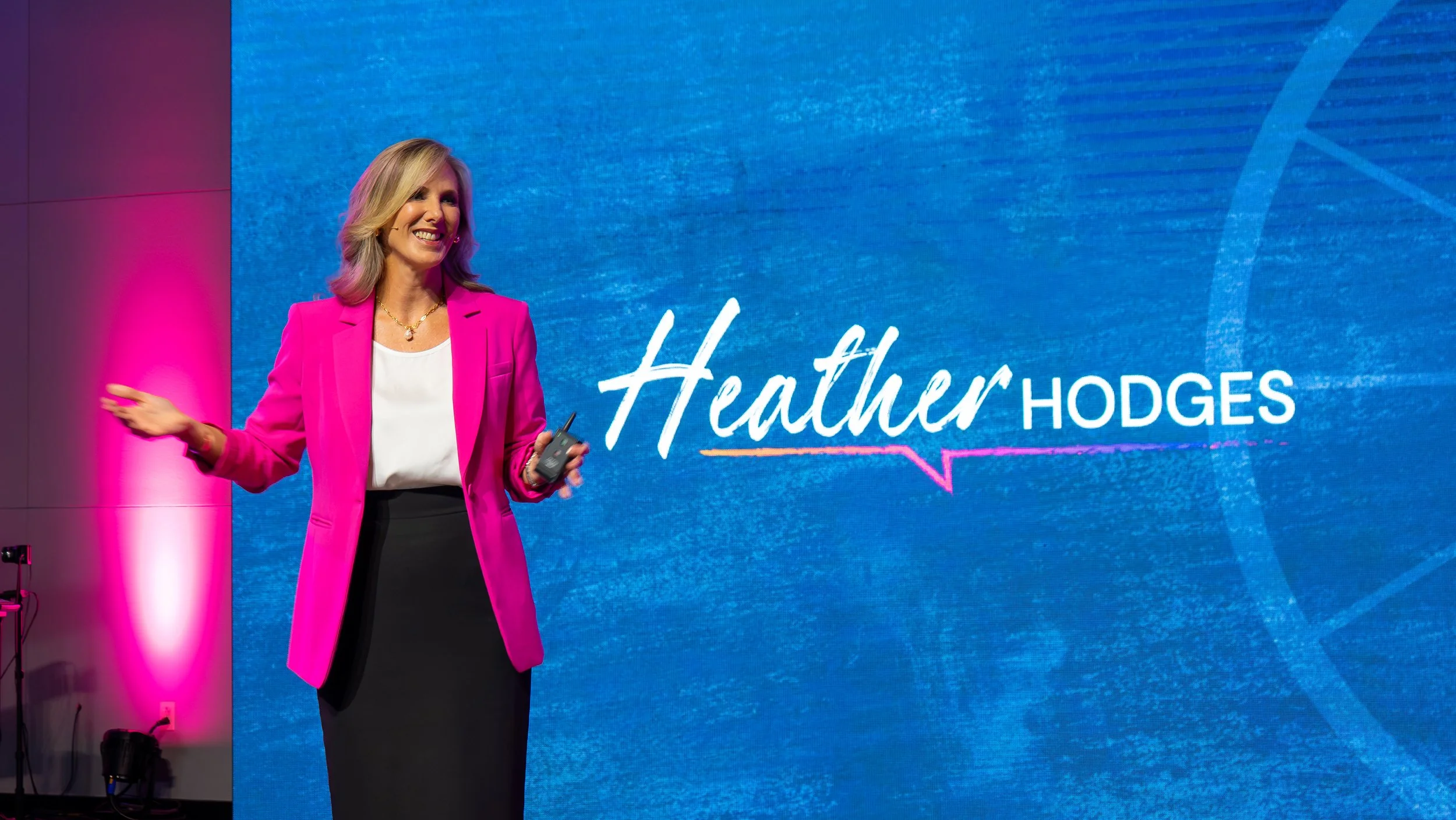 Heather Hodges speaking on stage, with her name displayed on the screen behind her.