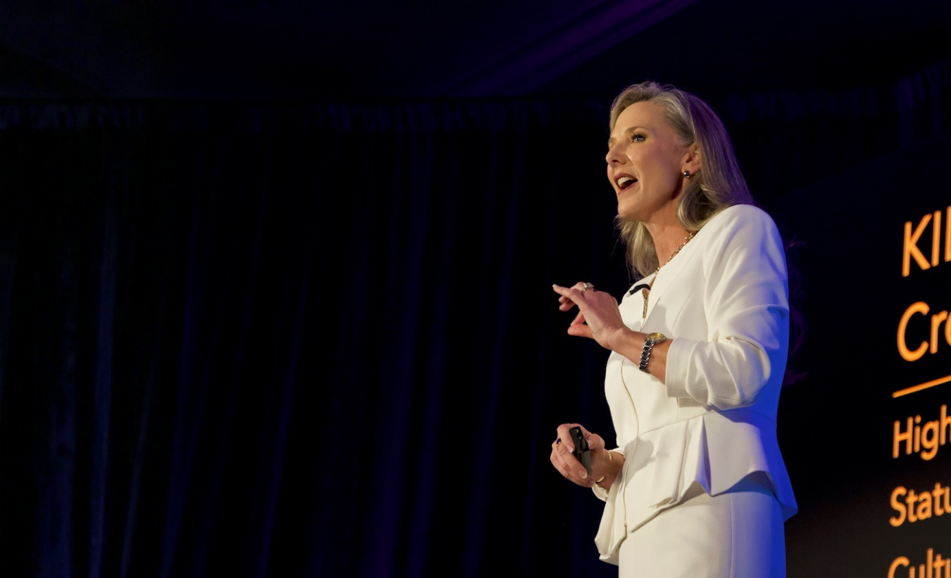 Heather Hodges speaking on stage in a white suit.