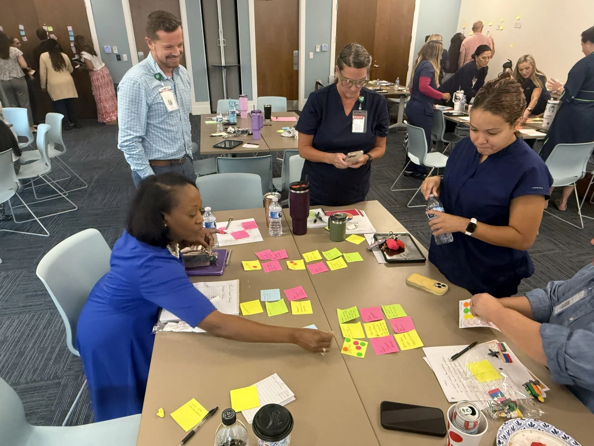People collaborating and brainstorming at a table with colorful sticky notes, notebooks, and drinks in a conference room during a workshop or training session.
