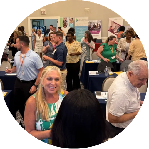 People mingling and networking at an indoor conference or business event with booths and banners in the background.
