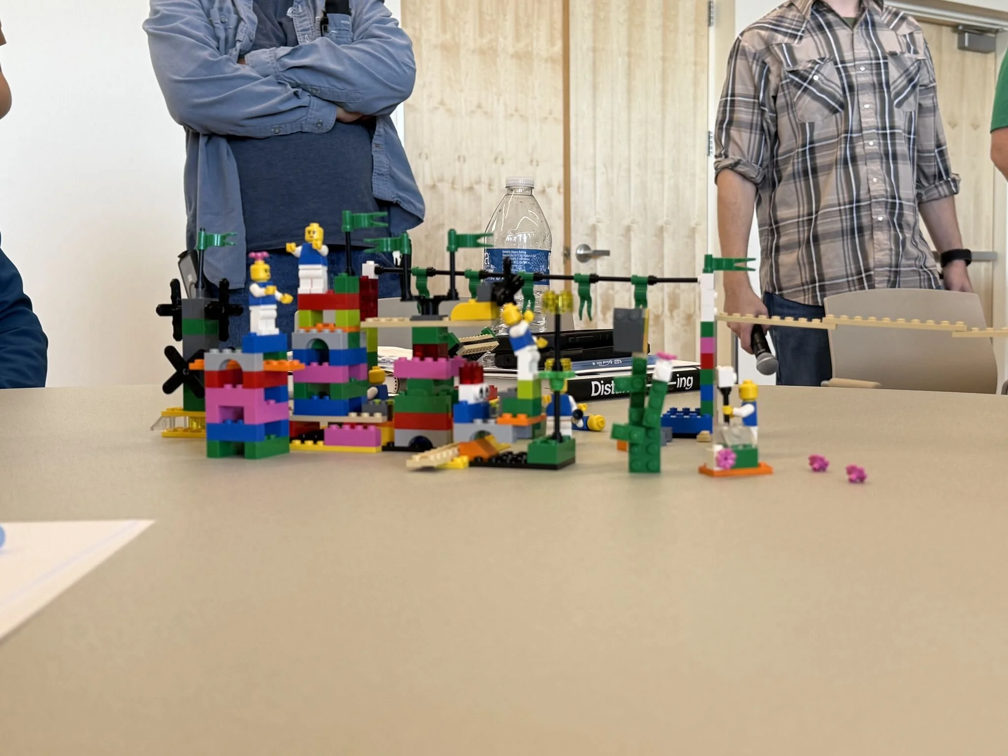 Colorful LEGO display on a table with two people standing behind it, one with crossed arms and another holding a microphone.