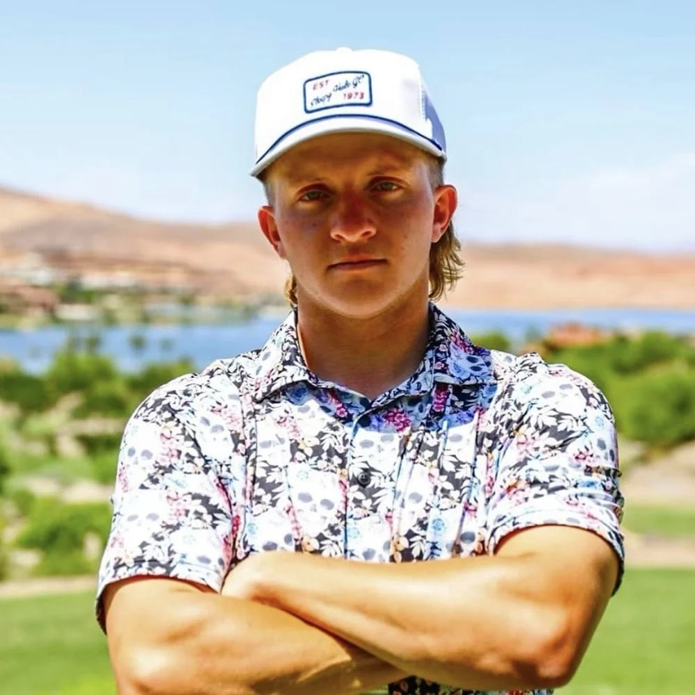 DOD KING (carter smith), wearing a white cap and a colorful floral shirt, standing outdoors with arms crossed. In the background, there is a body of water, green trees, and hills under a clear blue sky. Happy with grovemark media