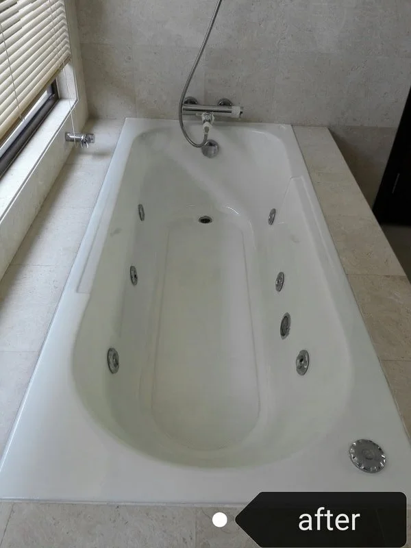 A white bathtub with multiple jets installed along the sides and bottom, located in a bathroom with light-colored tiles and a window with closed blinds.