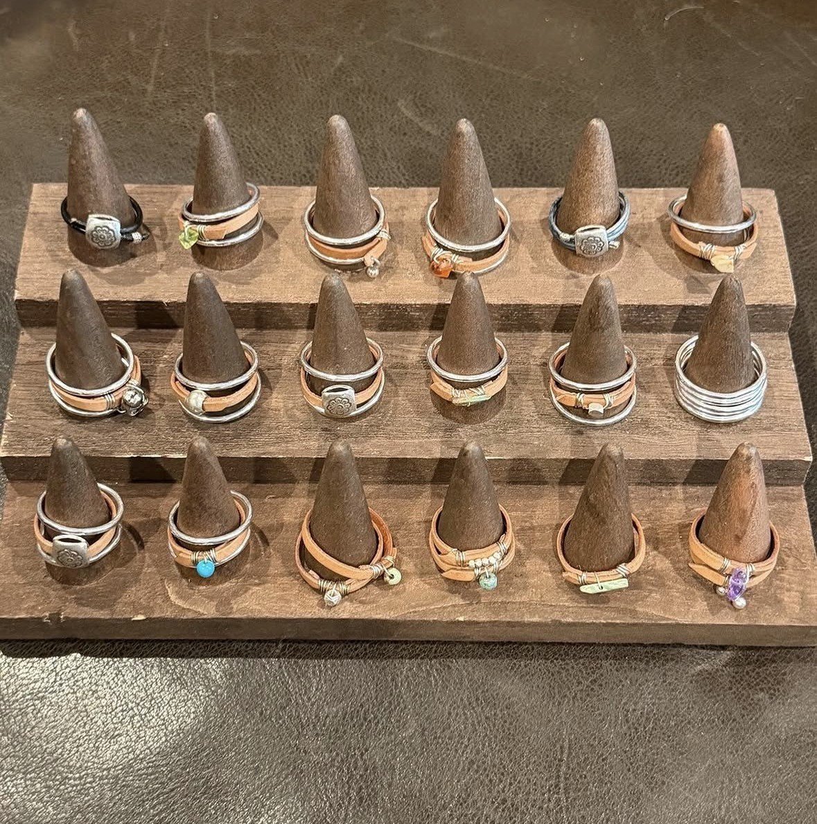 Display of multiple rings on cone-shaped stands organized on a wooden display stand.