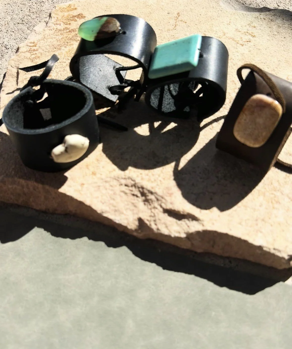 A collection of four black leather cuff bracelets with decorative stones placed on a rough, light-colored rock.