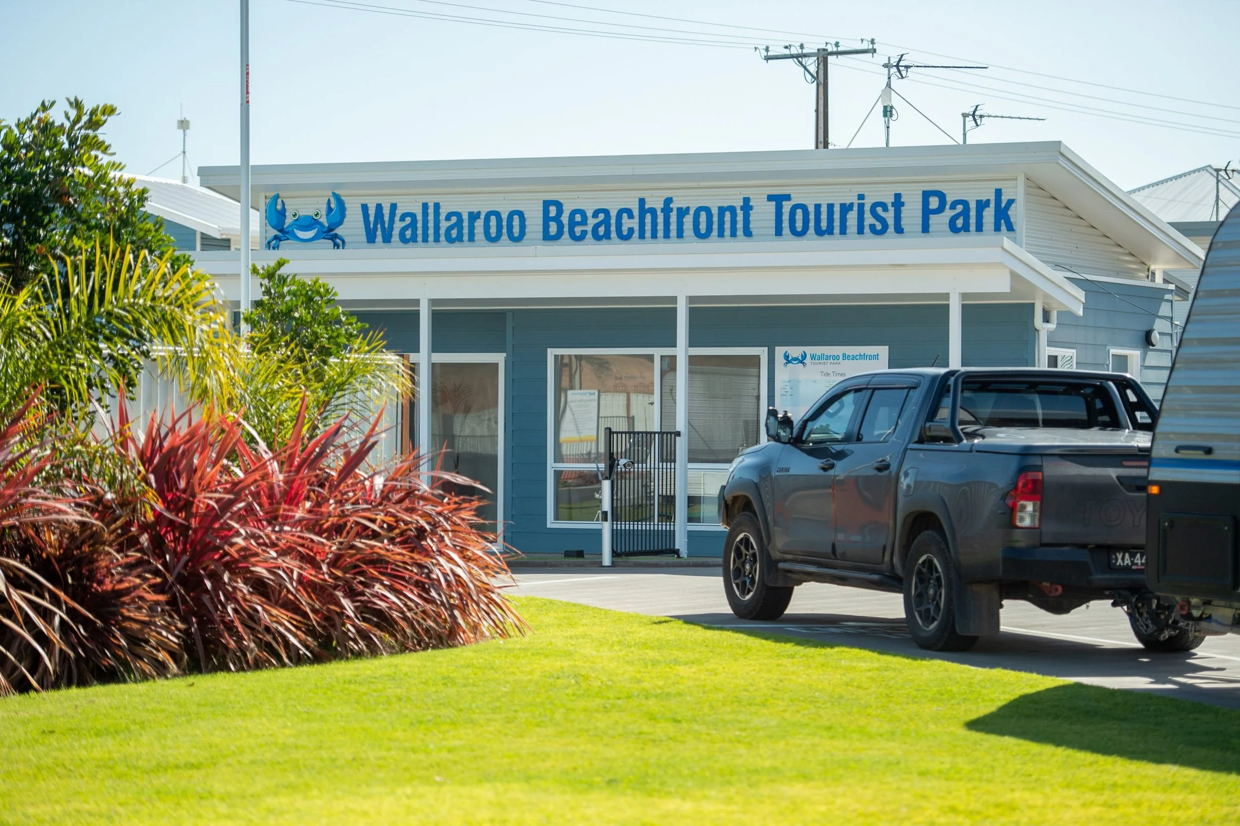 Sign for Wallaroo Beachfront Tourist Park with crab logo, parked vehicle, and surrounding greenery.